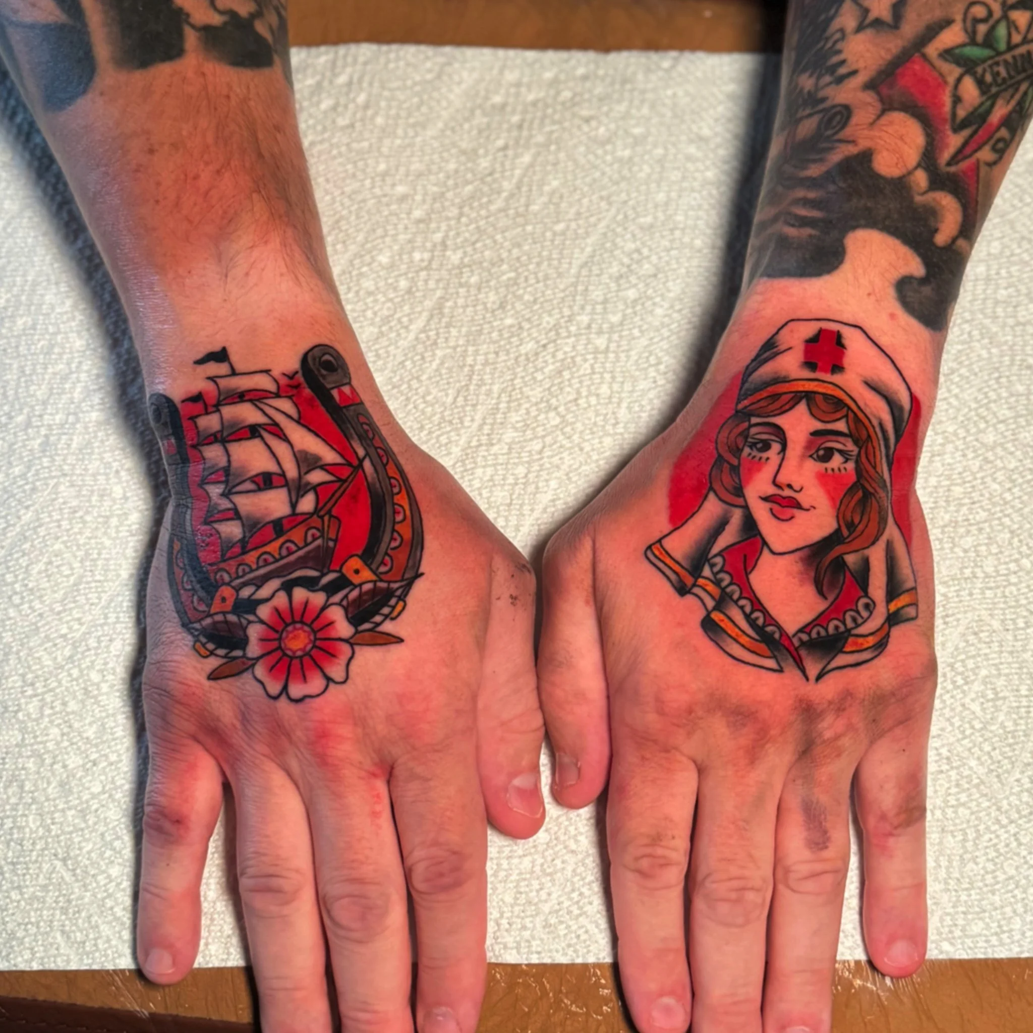 Close-up of tattoos on two forearms and hands, featuring superhero and comic book-style designs, with some skin redness visible.