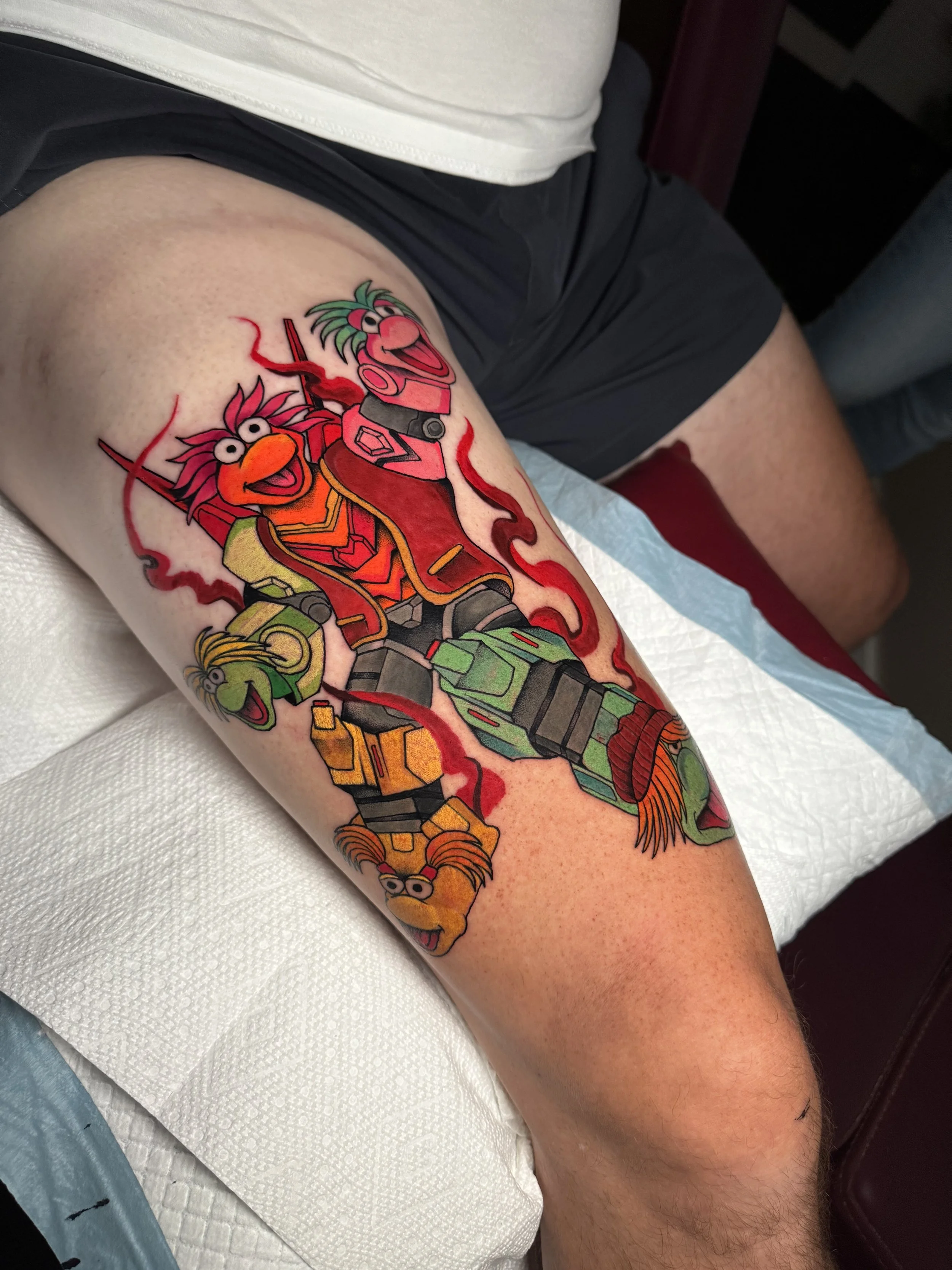 Colorful tattoo of Sesame Street characters on a person's leg, including Oscar the Grouch, Gonzo, and Fozzie Bear from The Muppets.