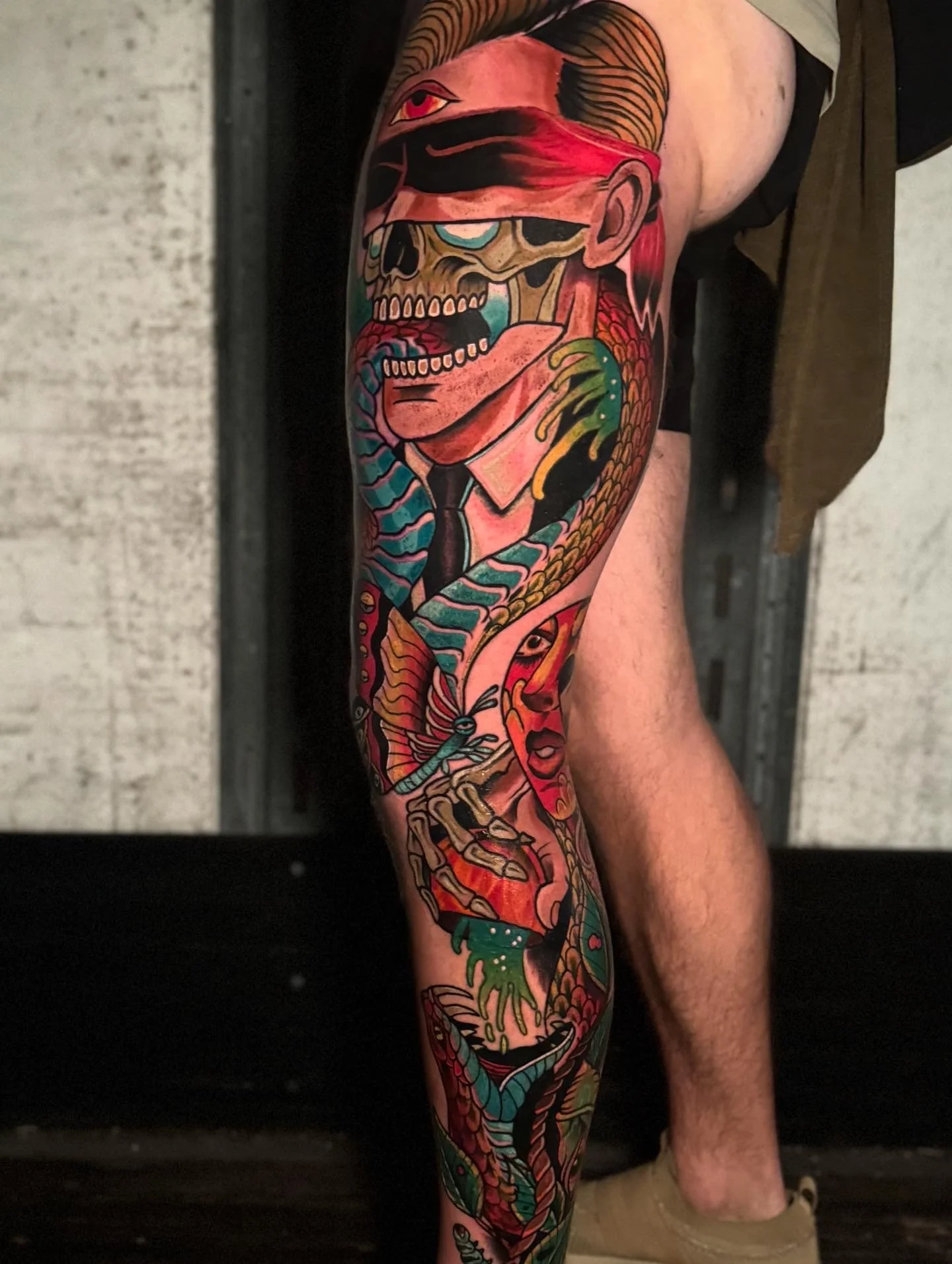 A colorful tattoo sleeve featuring a skeleton with a red bandana, multiple snakes, and various vibrant elements covering the person's arm.