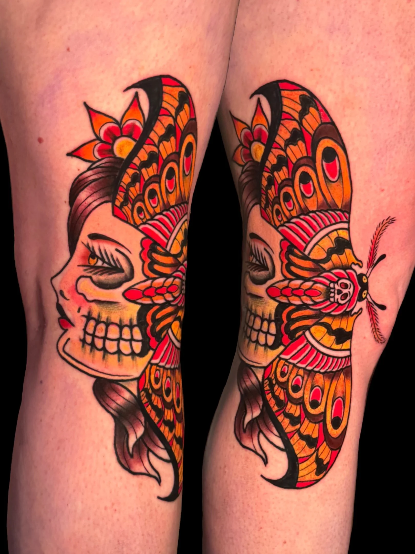 Colorful tattoo of two orange, black, and red butterflies with floral and skull designs on upper arms.