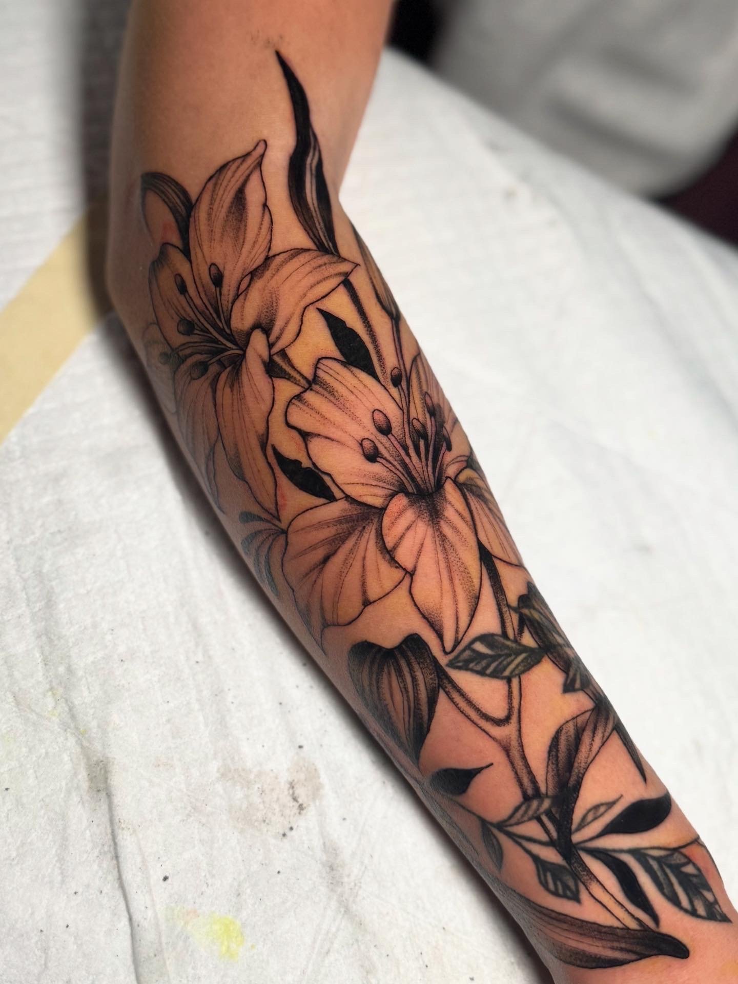 A tattoo of orange lilies with black outlines and leaves on a person's forearm.