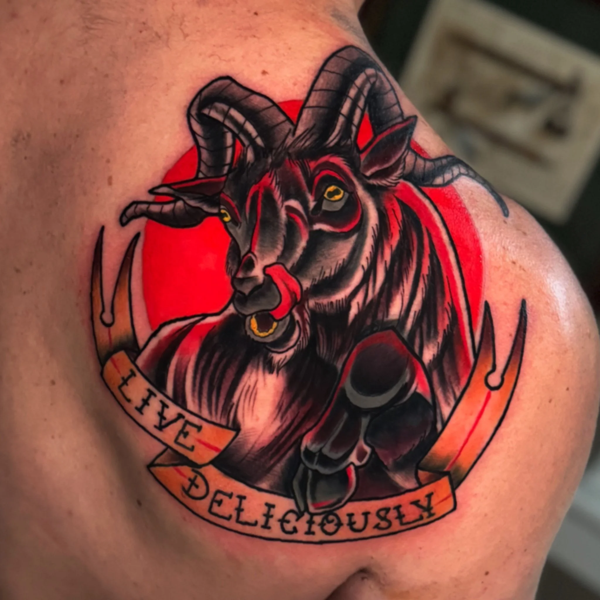 Close-up of a tattoo on skin featuring a black spider with detailed legs and yellow eyes, set against a red circular background with black text around it.