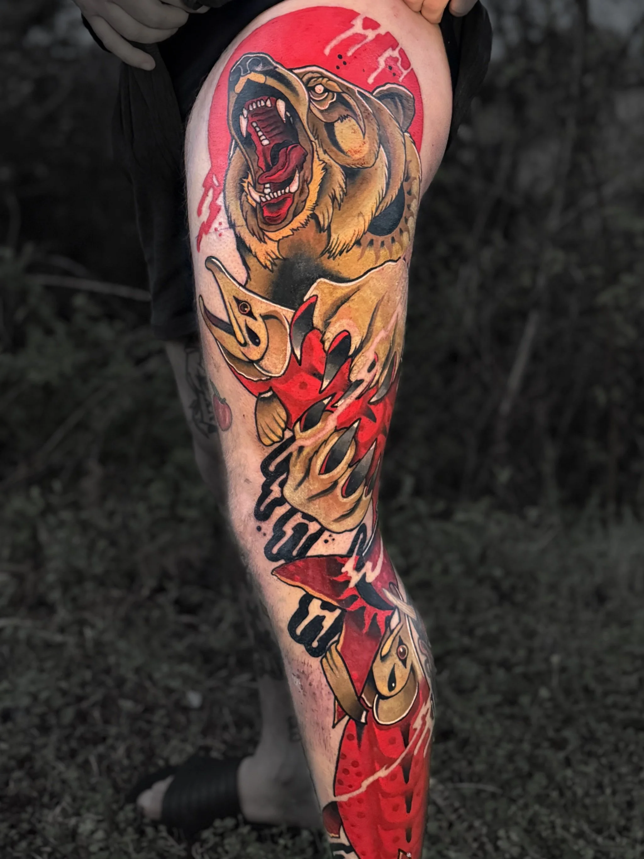 Tattoo of a roaring lion on a person's thigh, with red, orange, and yellow colors and black outlines, including the word 'fear' written above the lion's head.