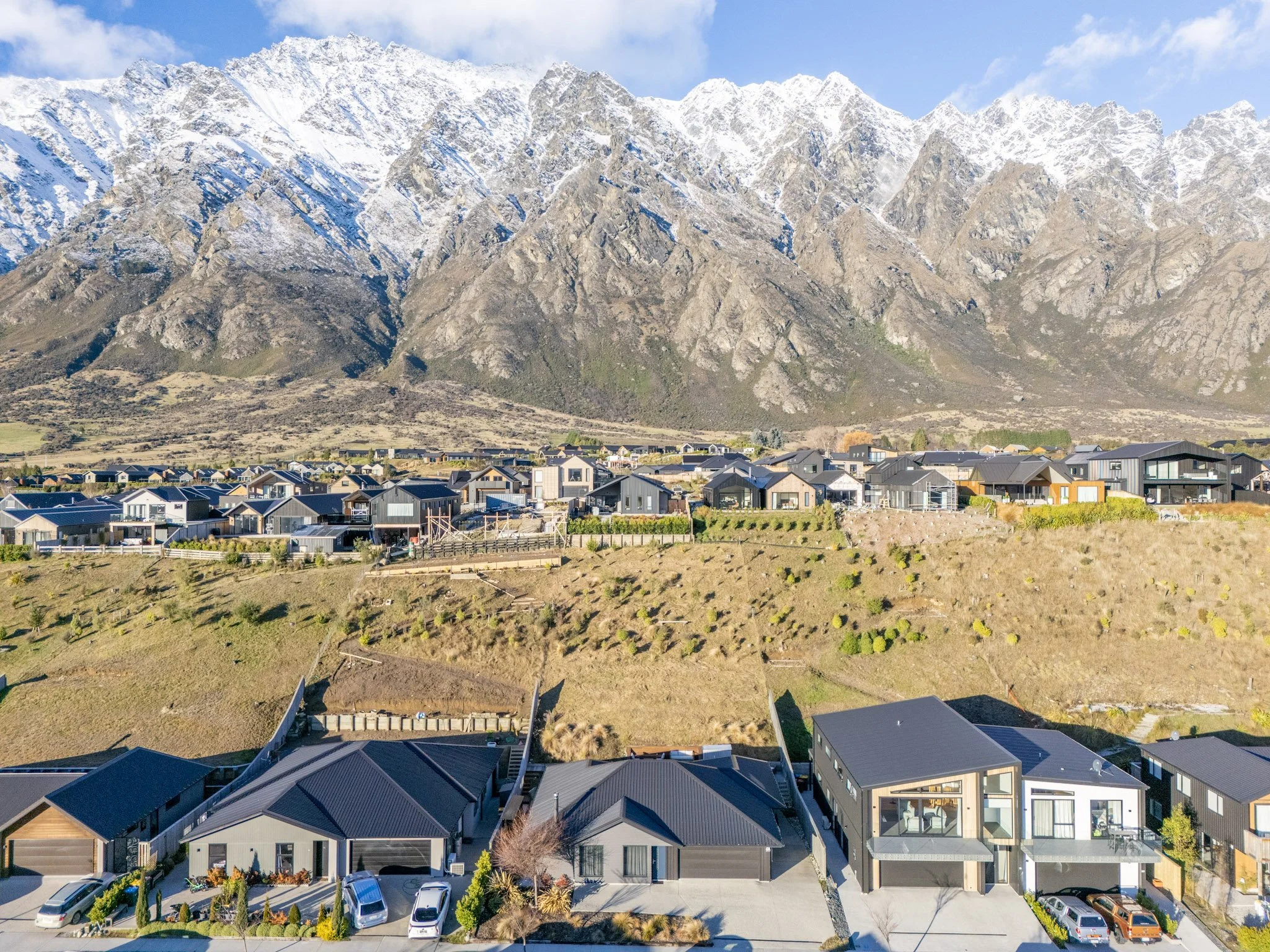A residential neighborhood with modern houses at the base of a snow-capped mountain range.