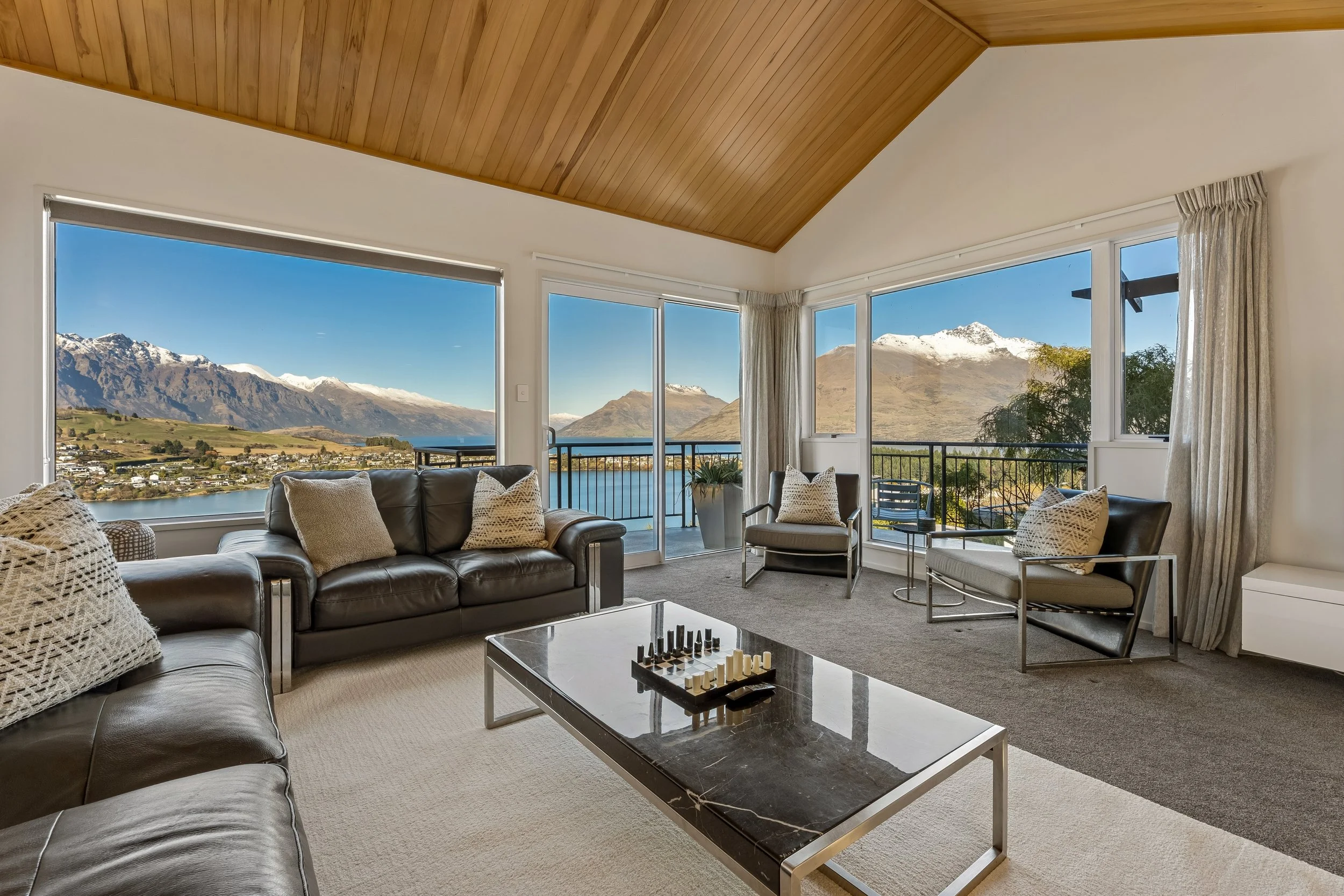 Living room with large windows showing a mountain and lake view, sofas and chairs, a coffee table, and curtains.