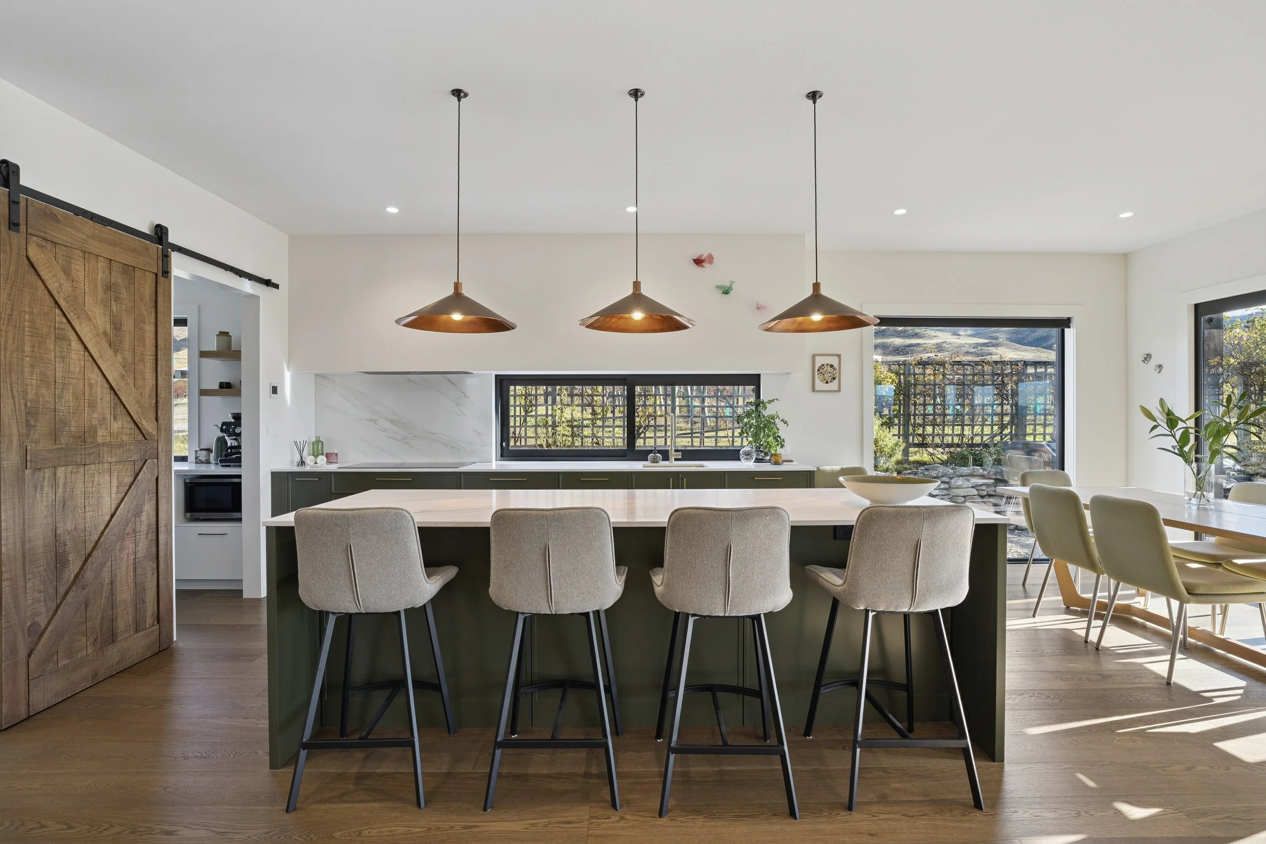 Modern kitchen and dining area with hanging pendant lights, a large window, and a sliding wooden barn door.