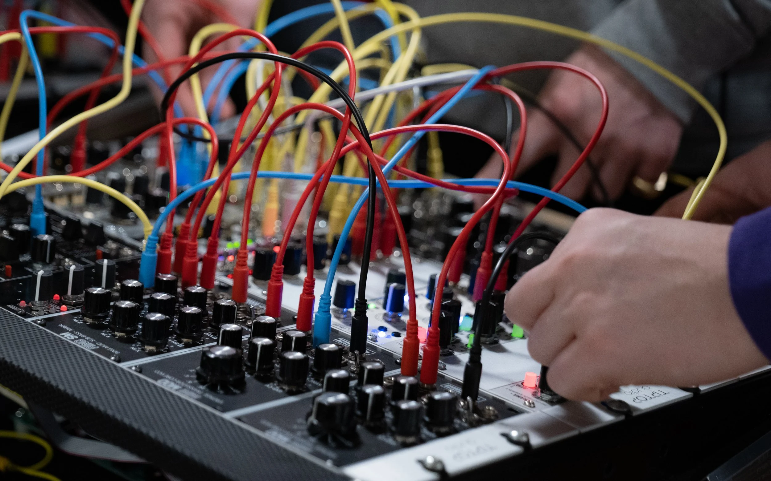 Hands adjusting knobs and connecting cables on a modular synthesizer.