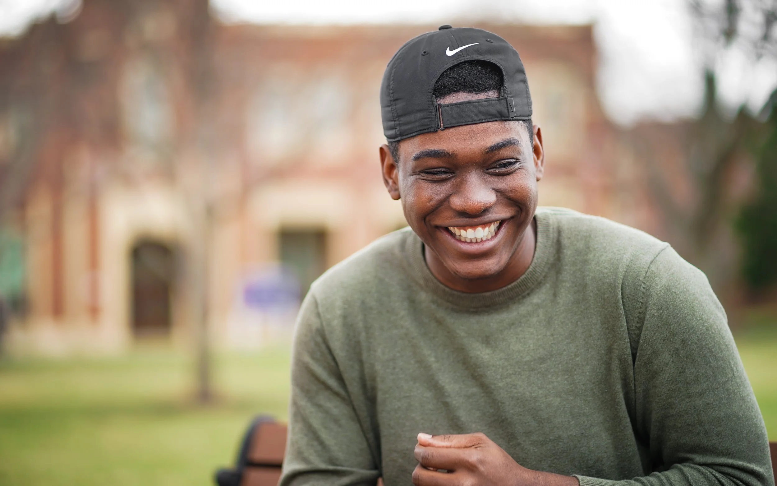 Smiling person wearing a green sweater and black Nike cap outdoors.