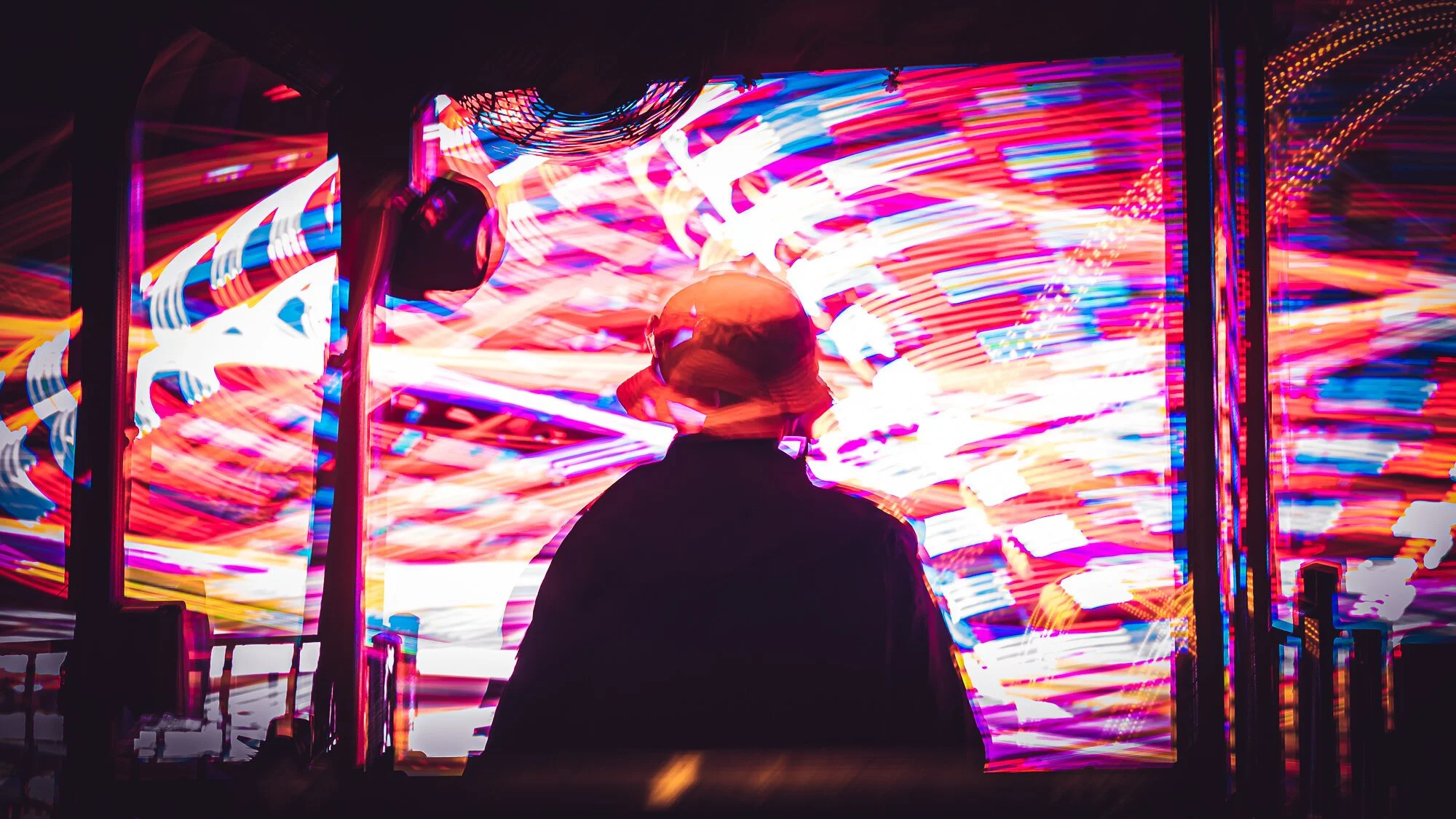 Person in hat silhouetted against colorful, blurred lights at a carnival.