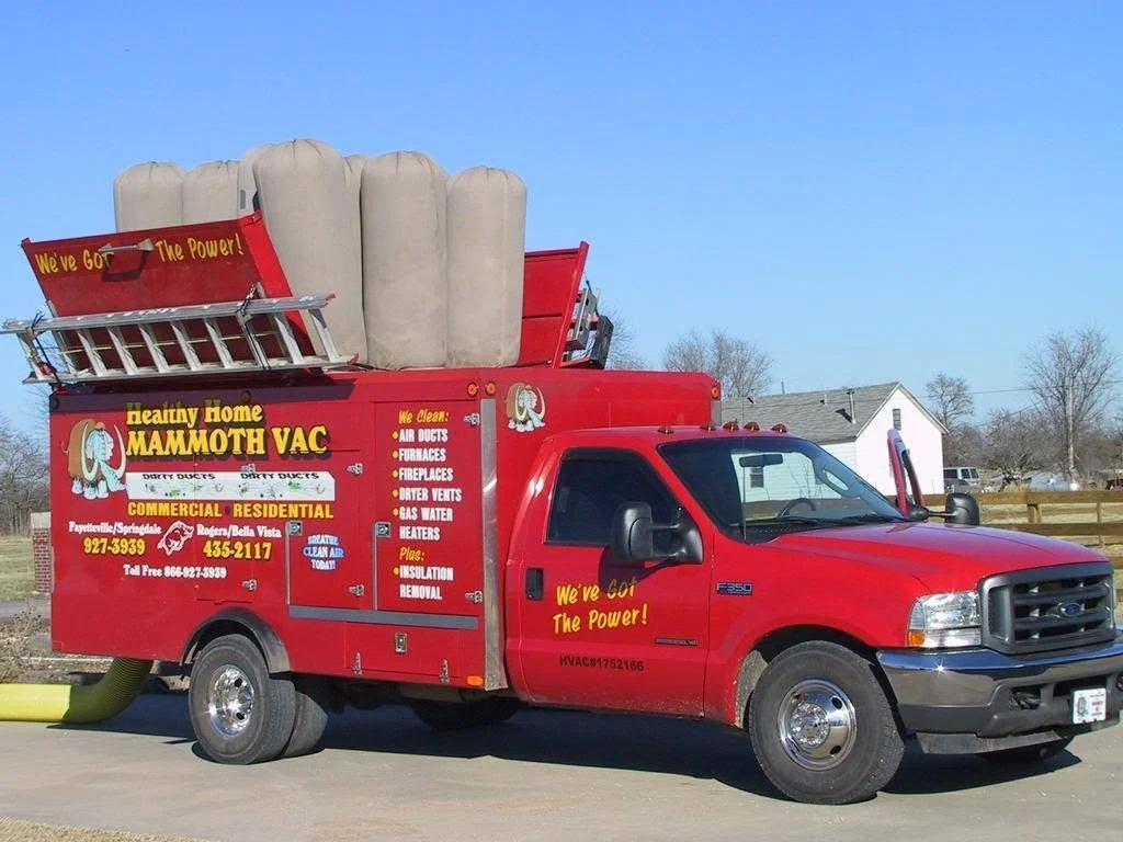 Red service truck with company's name 'Heady Home Mammoth Vac,' advertising indoor air duct cleaning, fireplaces, and HVAC services, with a large beige vacuum or duct cleaning machine on top and yellow hoses at the rear, parked outdoors on a clear day.