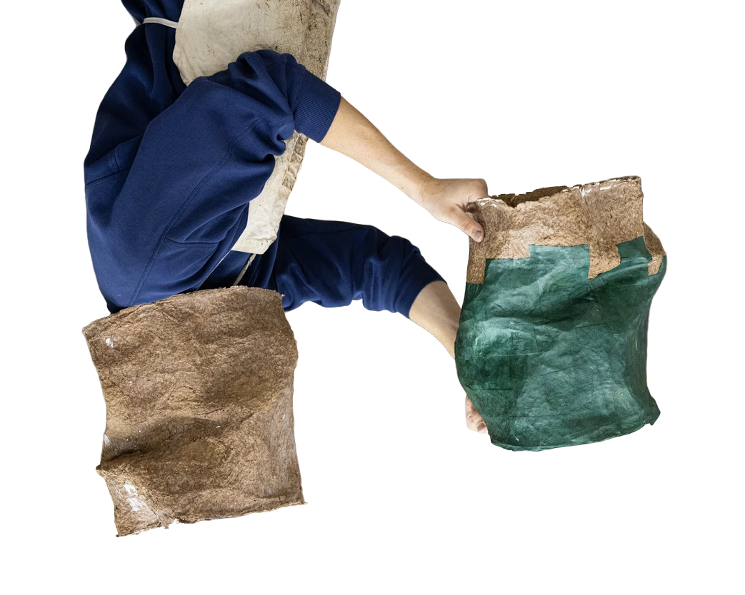 Person in blue pants and a beige shirt handling two large paper bags, one brown and one green, filled with soil or dirt.