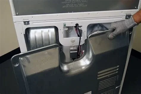 Close-up of a person wearing a gray glove working on the back of a large white industrial machine, revealing metallic components inside.