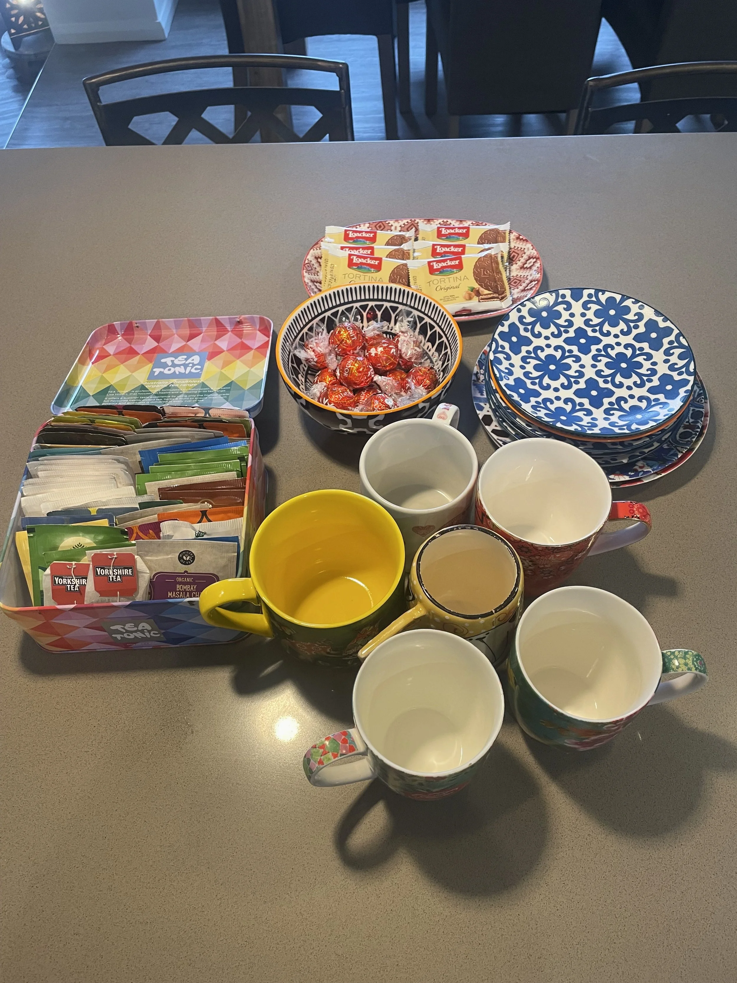 A table with various colorful mugs, bowls, plates, and packets of tea, chocolates, and candies.