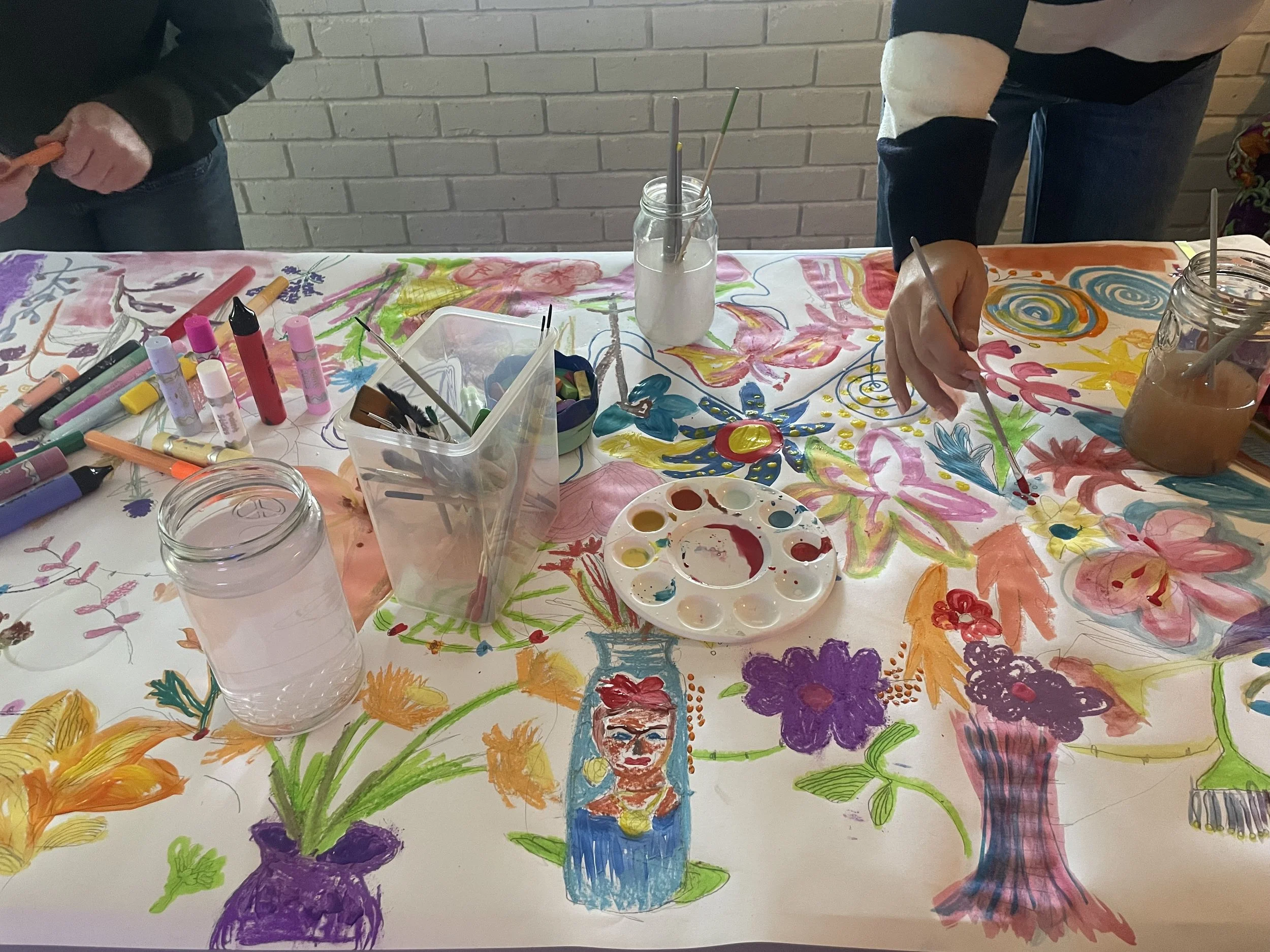 People painting flowers and faces on a large canvas with various paints and brushes.