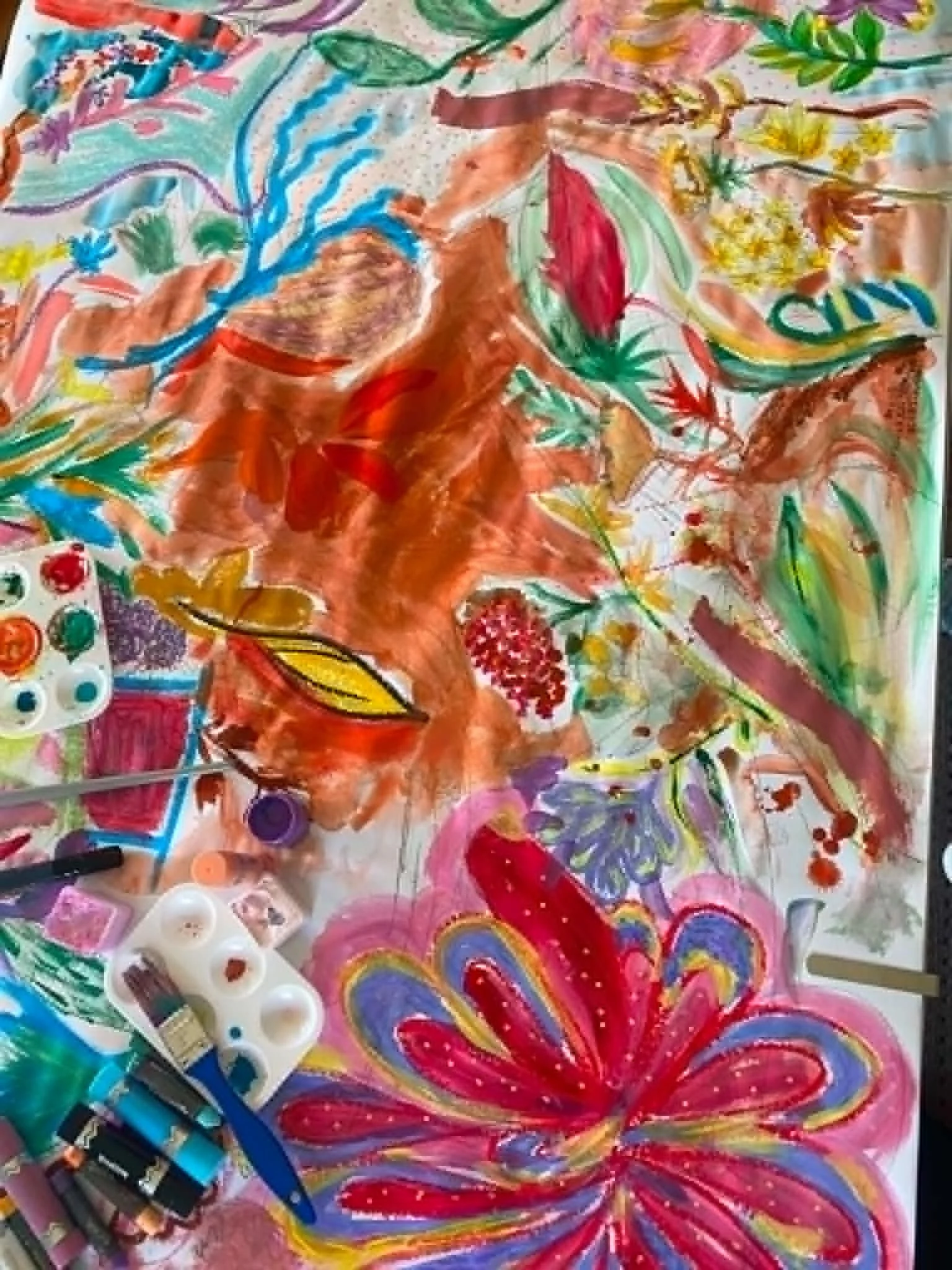 Colorful abstract drawing of flowers, leaves, and flowing shapes in various bright colors, with art supplies like markers and paint bottles nearby.