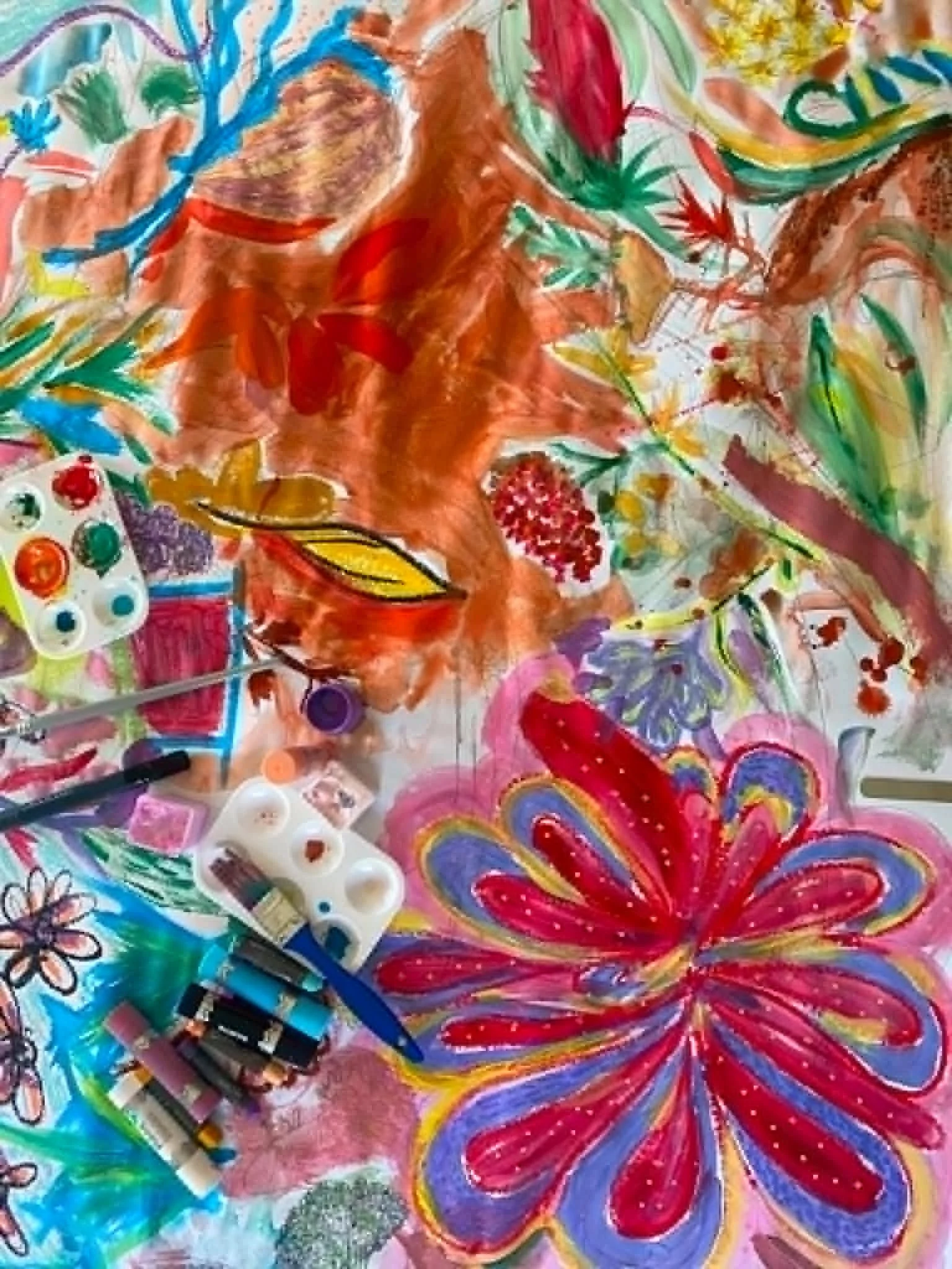 Colorful abstract artwork with flowers, patterns, and various bright colors including red, blue, green, yellow, and pink. There are also some art supplies and tools visible, like pens and markers, indicating a creative workspace.