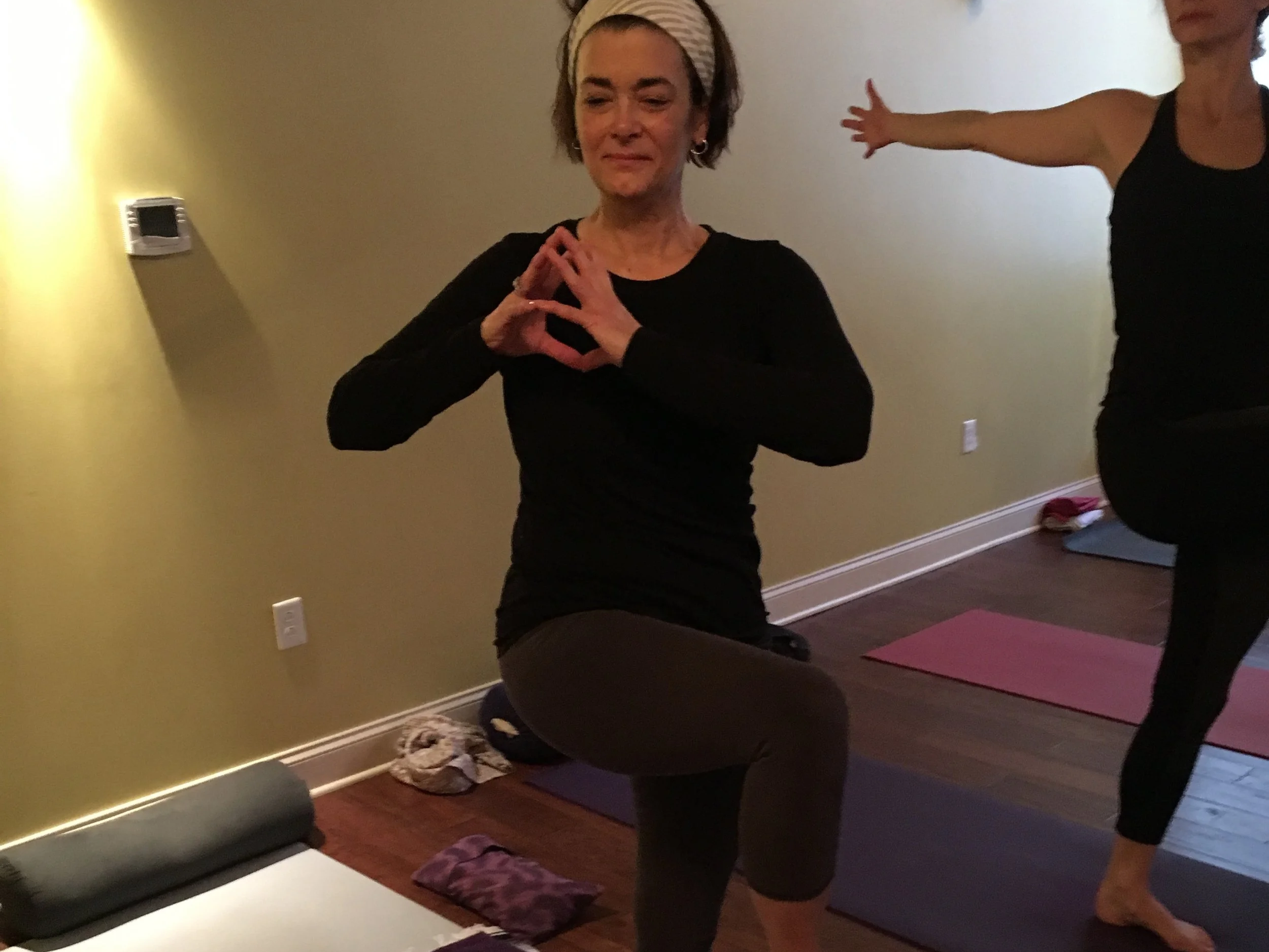 A person standing on one leg with hands at heart center in a yoga class