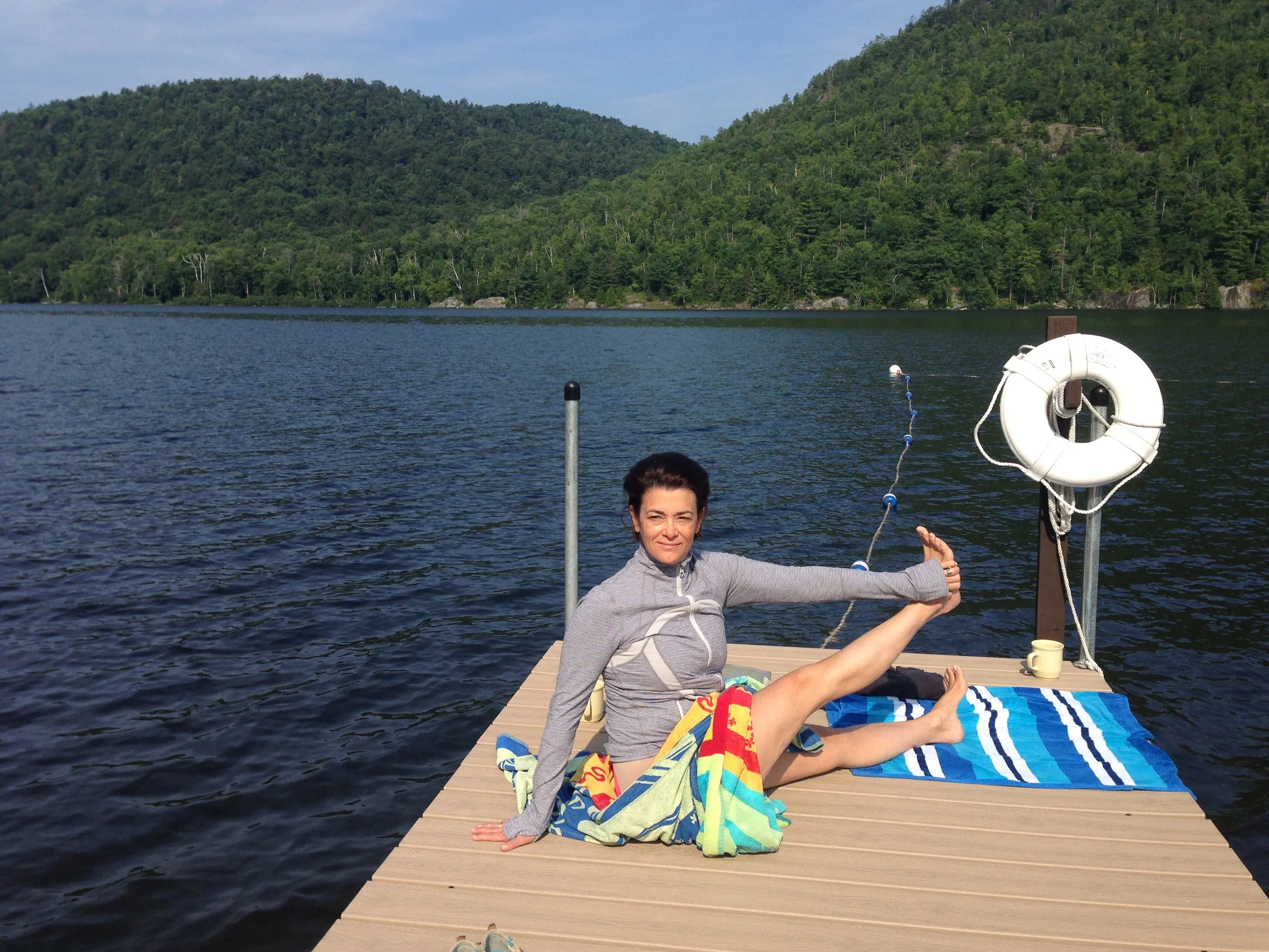 A person seated on a dock by a lake, stretching in a yoga pose
