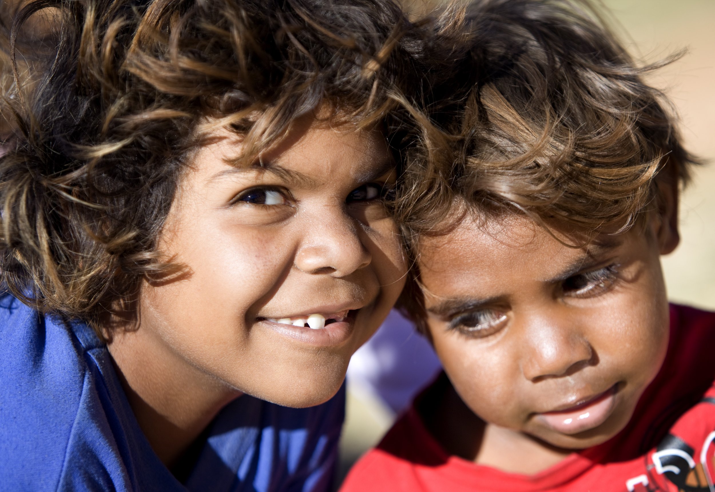 Close-up of two children smiling and leaning close together, outdoors