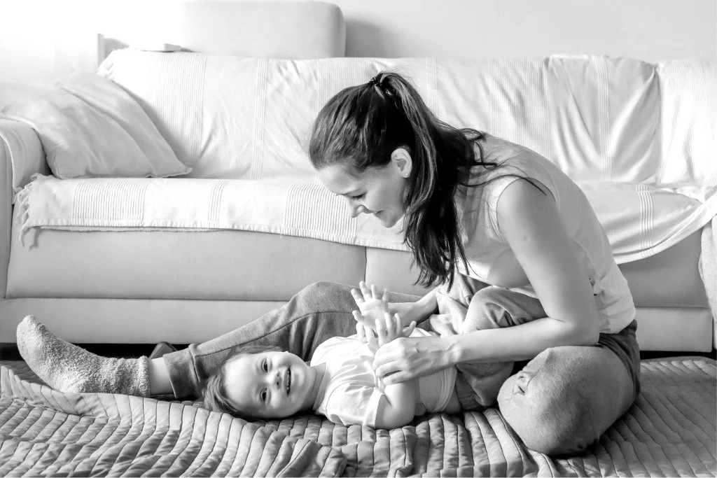 A woman playing with a young girl on the floor in a living room.