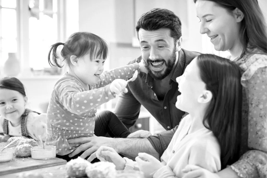Family celebrating a birthday with children and adults smiling and laughing around a table with cupcakes.