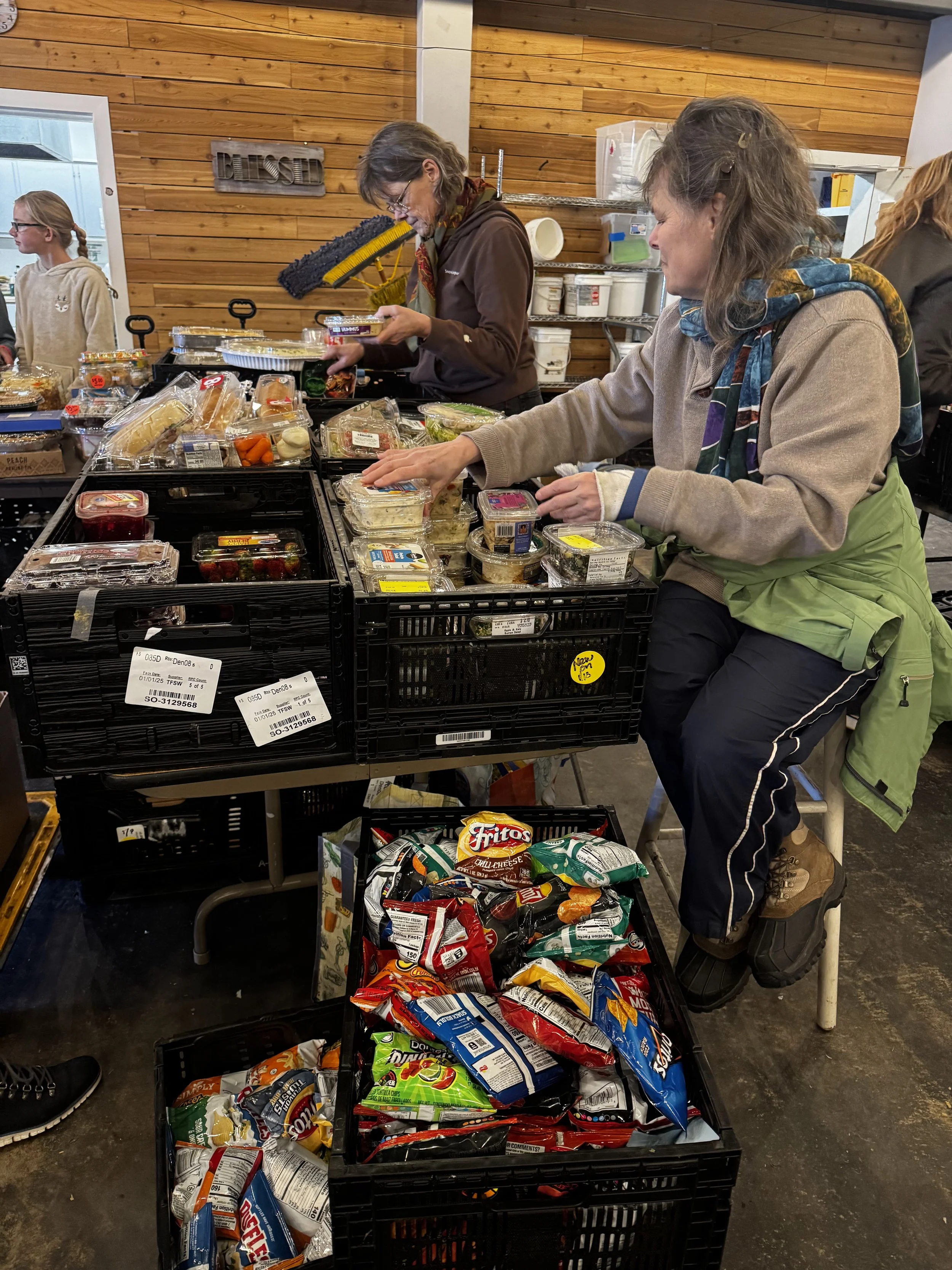 People shopping for snacks and groceries at a store, with various snack bags and pre-packaged food items on display.