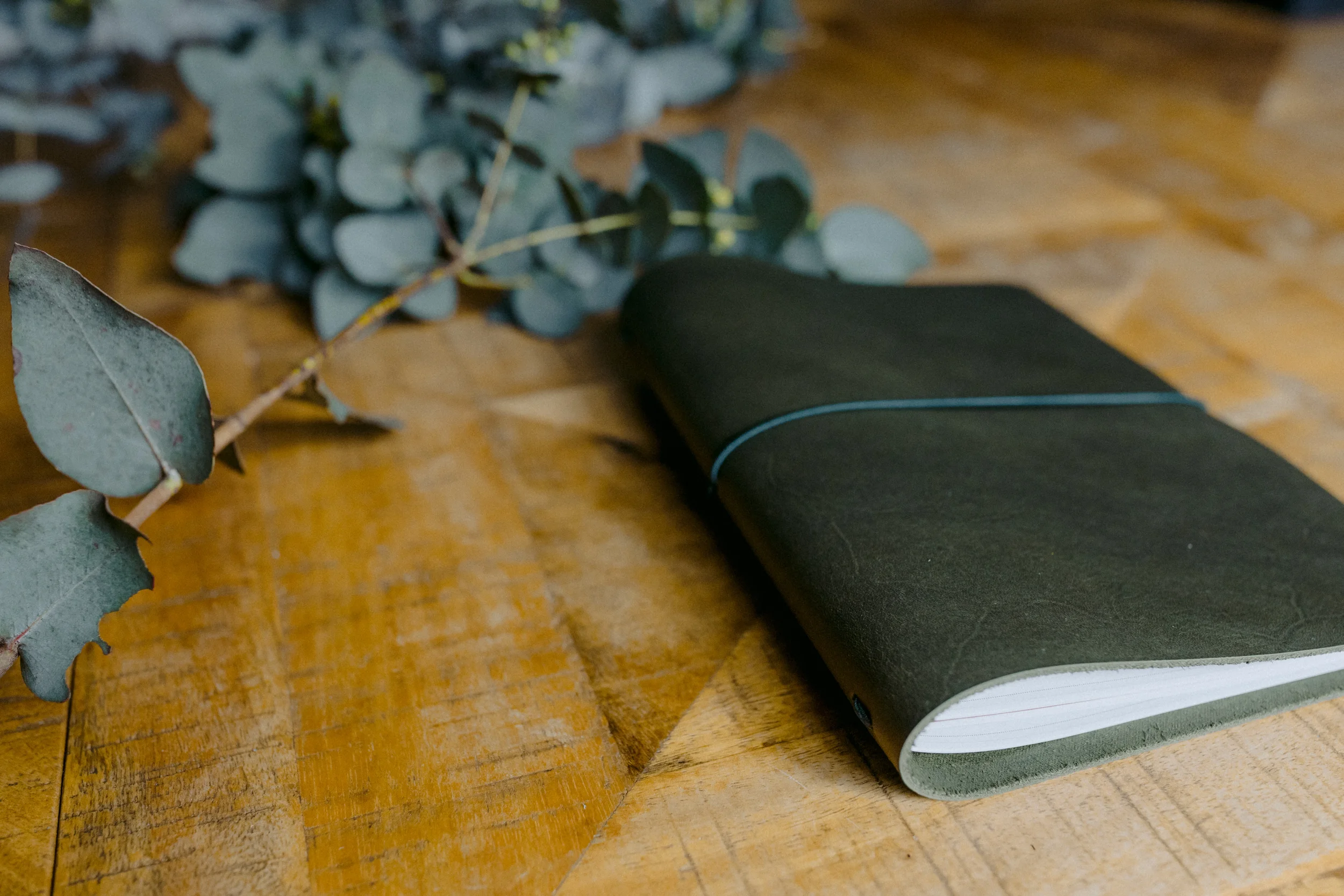 A black yoga mat rolled up on a wooden surface next to fallen eucalyptus leaves and a white sneaker with a green sole.