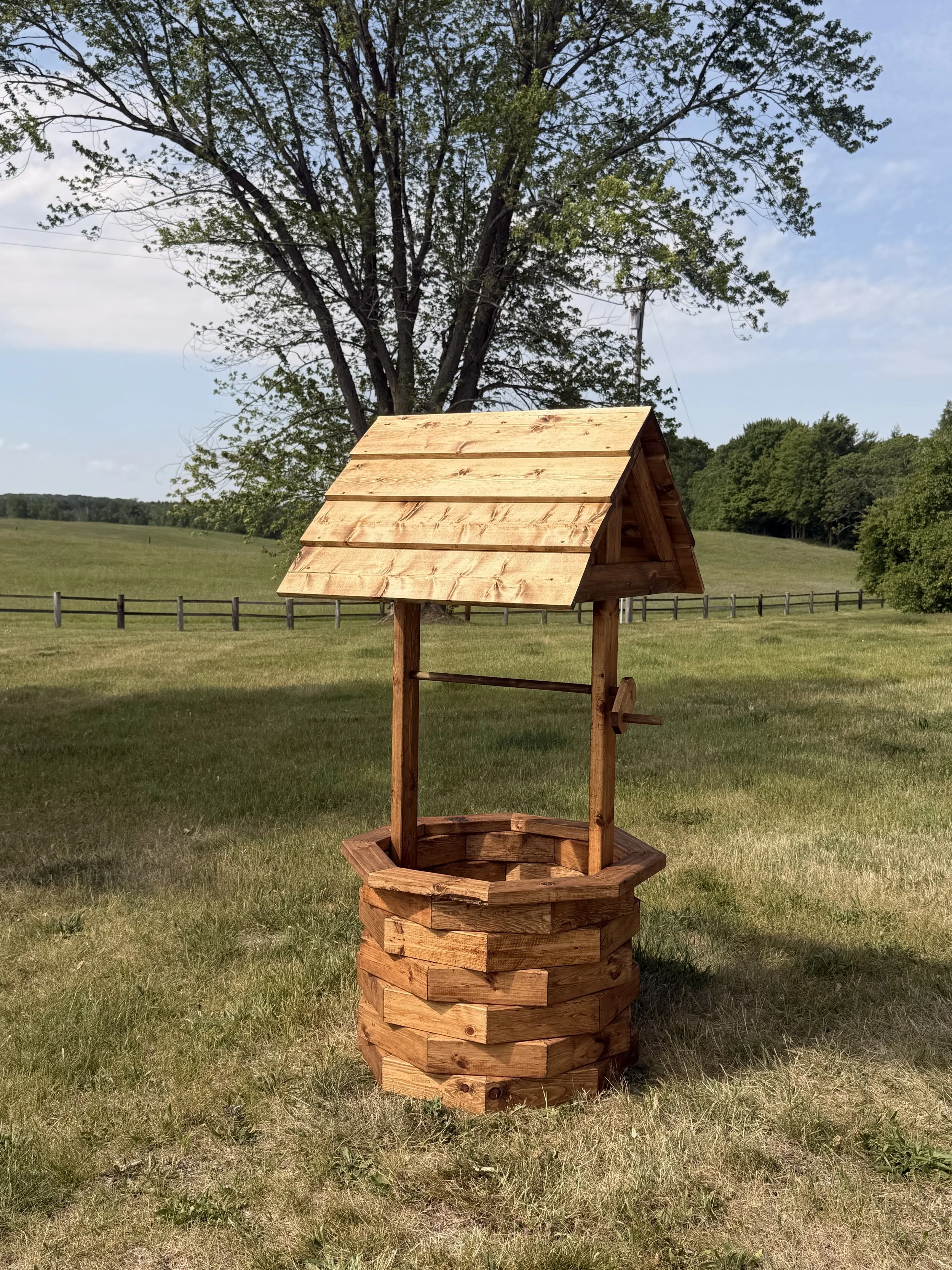 A stained wooden wishing well sitting on a grassy lawn.