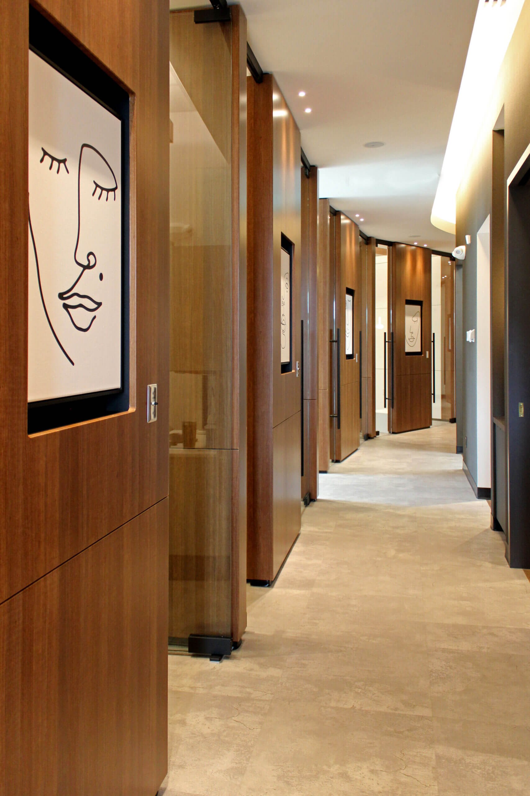 Hallway with wooden room dividers, framed artwork featuring a minimalist face, and warm lighting.