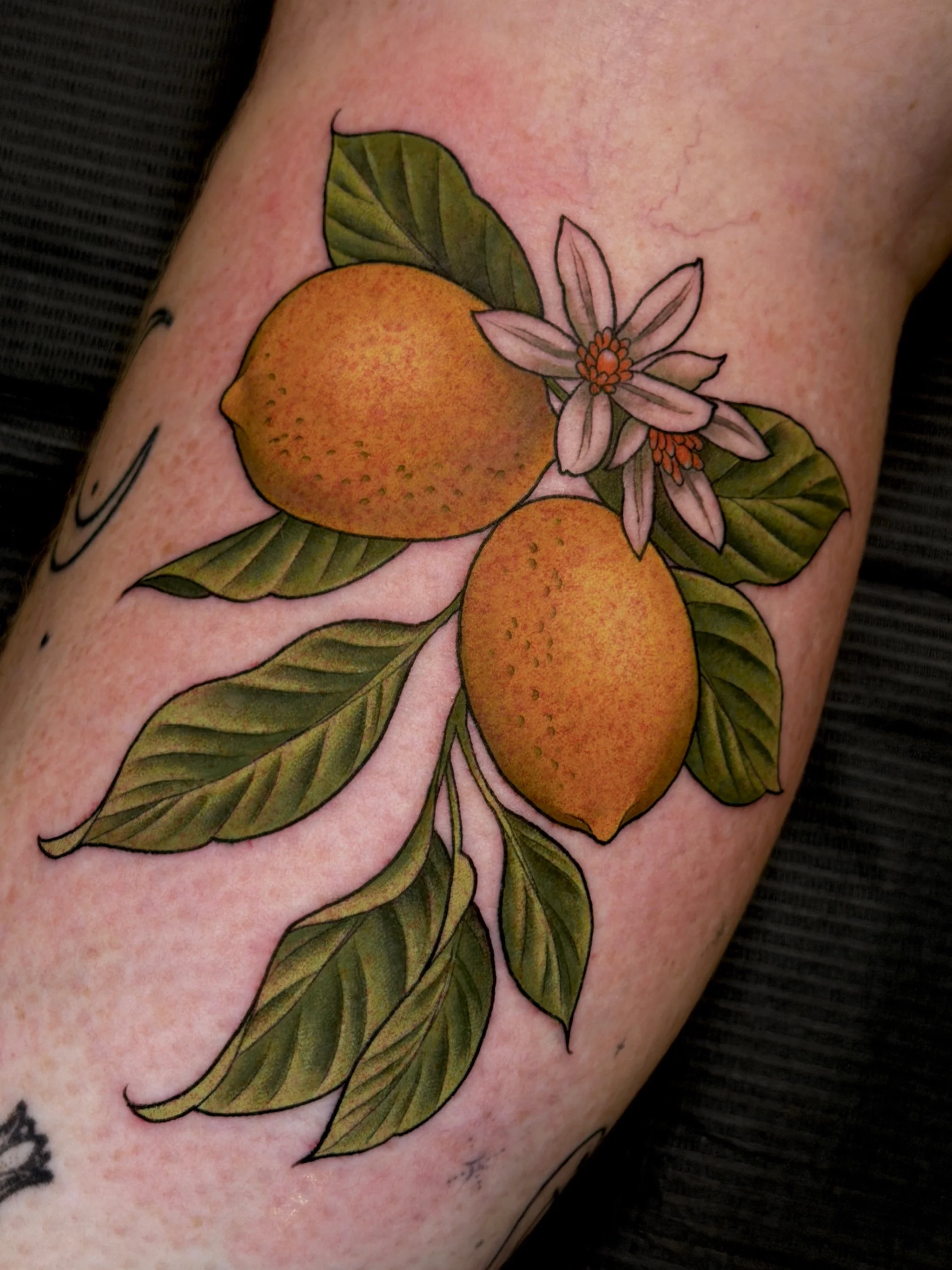 Tattoo of two oranges with leaves and a flower on the skin.