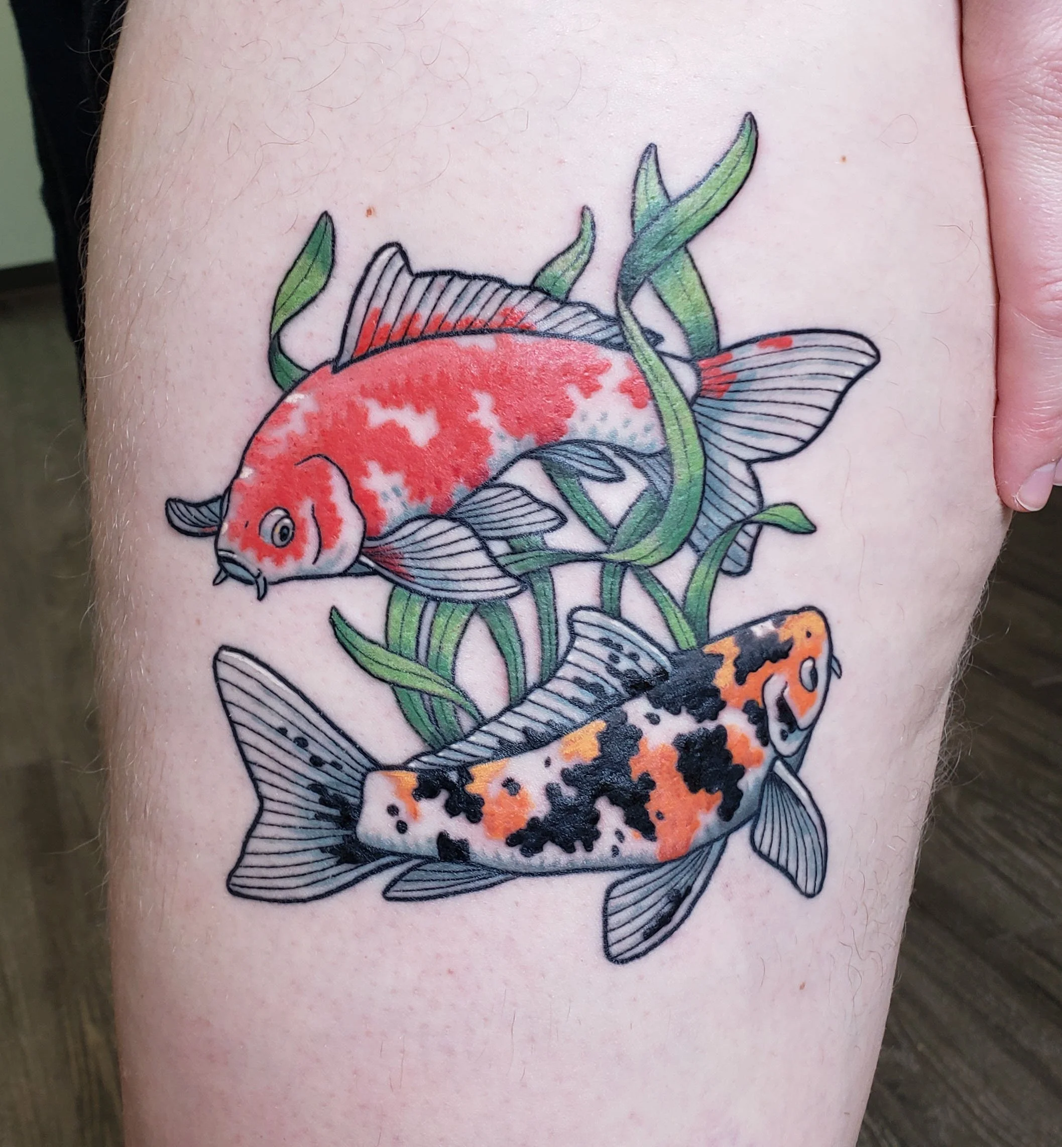 Colorful tattoo of a koi fish with green leaves and orange and black accents on skin.