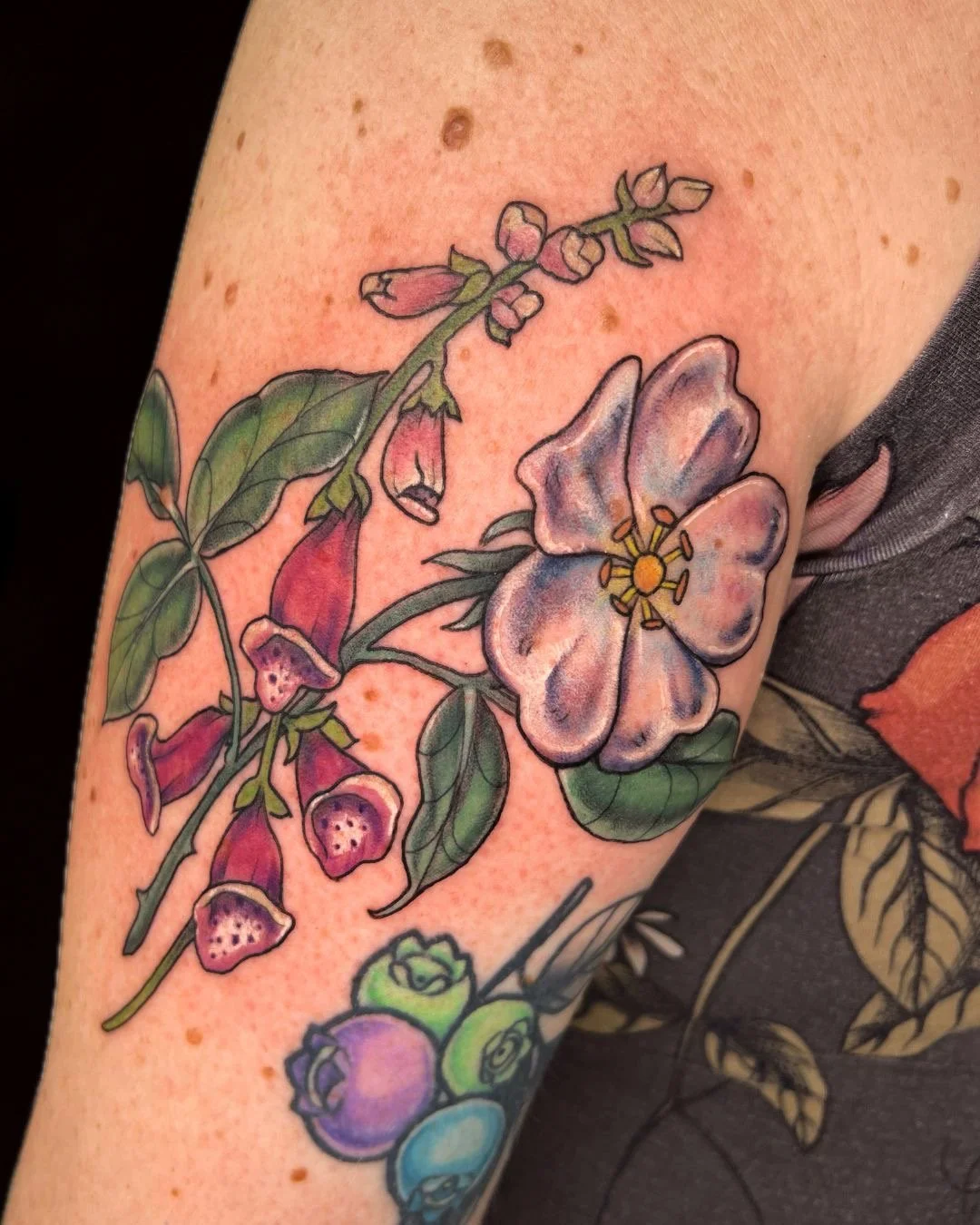 Colorful floral tattoo on person's arm featuring pink and purple flowers with green leaves.