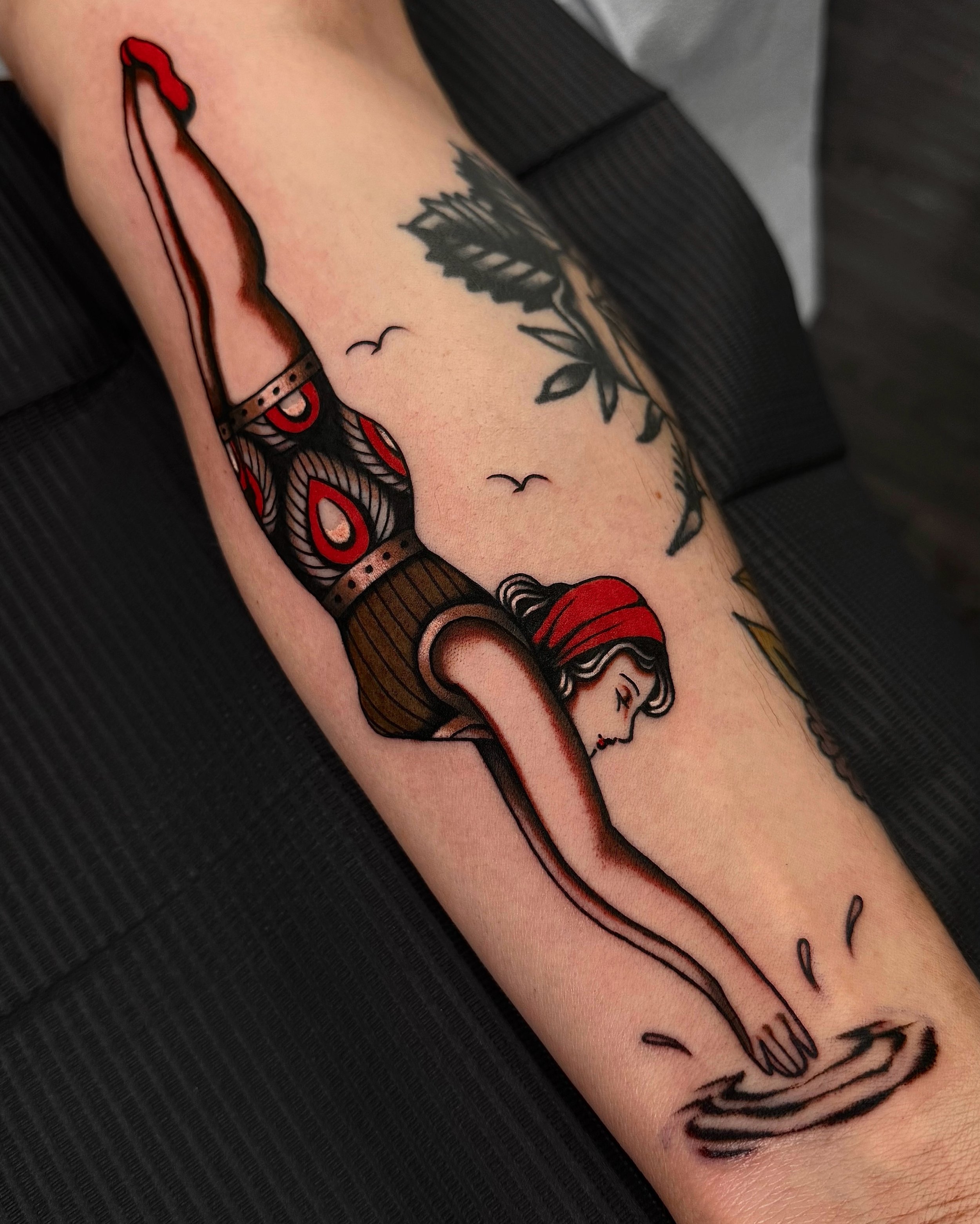 Tattoo of a woman with a headscarf, possibly depicting Little Red Riding Hood, and a length of text on the forearm.