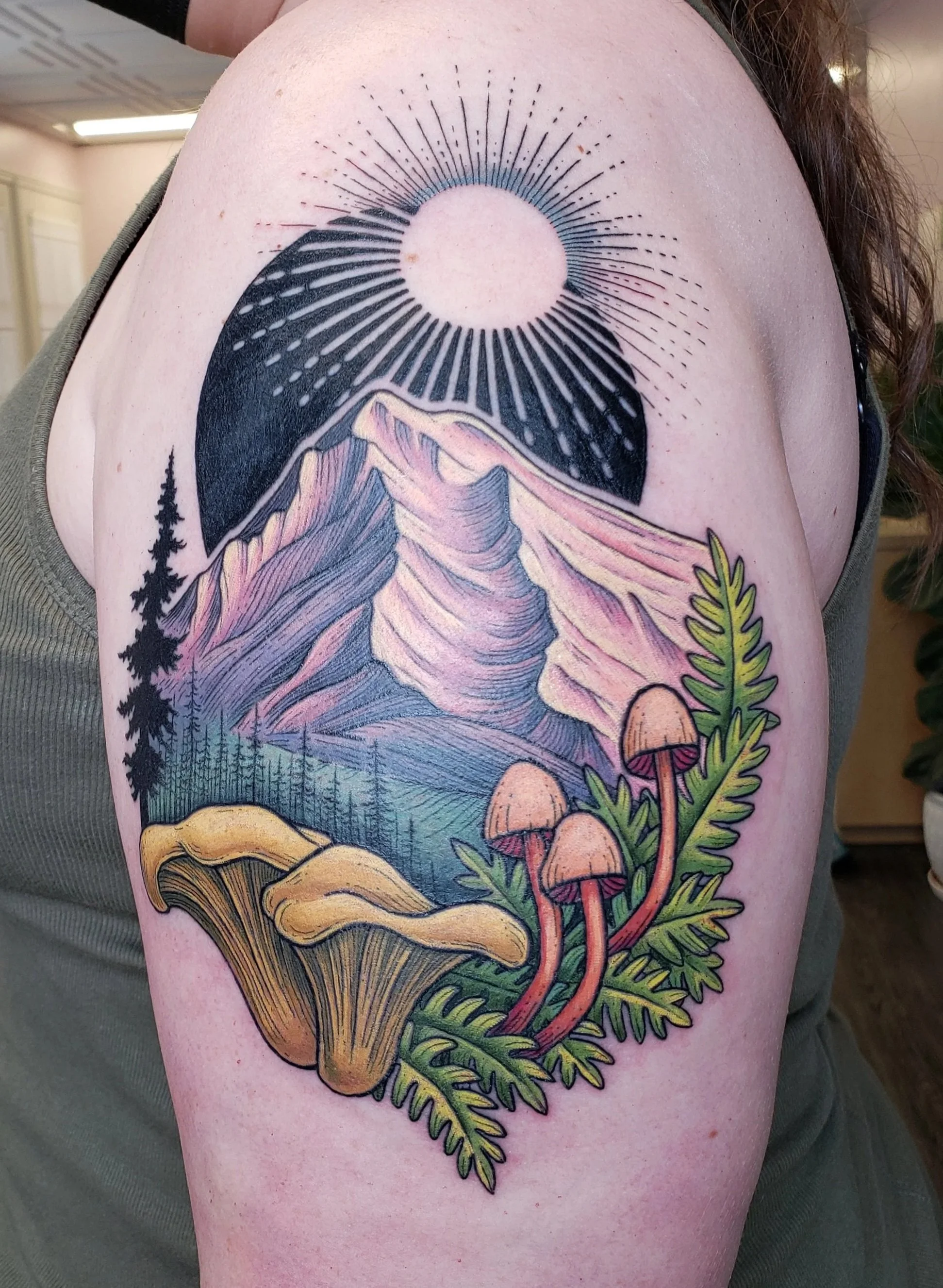 Colorful tattoo of a mountain landscape with trees and mushrooms on a person's upper arm.