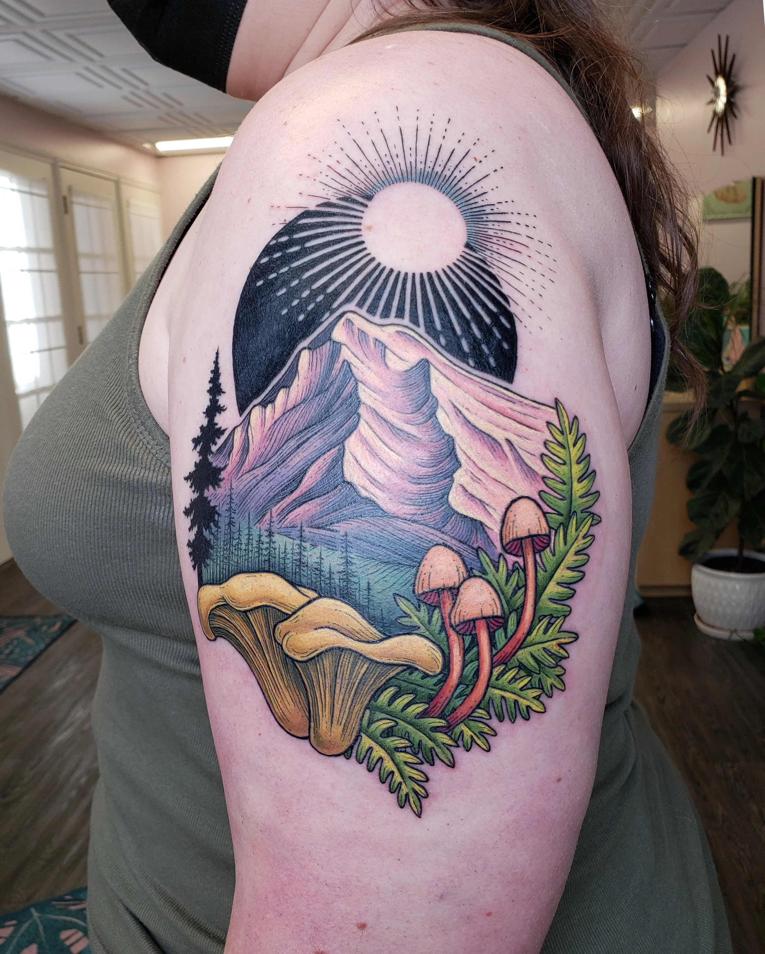 Colorful tattoo of a mountain scene with trees, a mushroom, and a moon on a person's shoulder and upper arm.