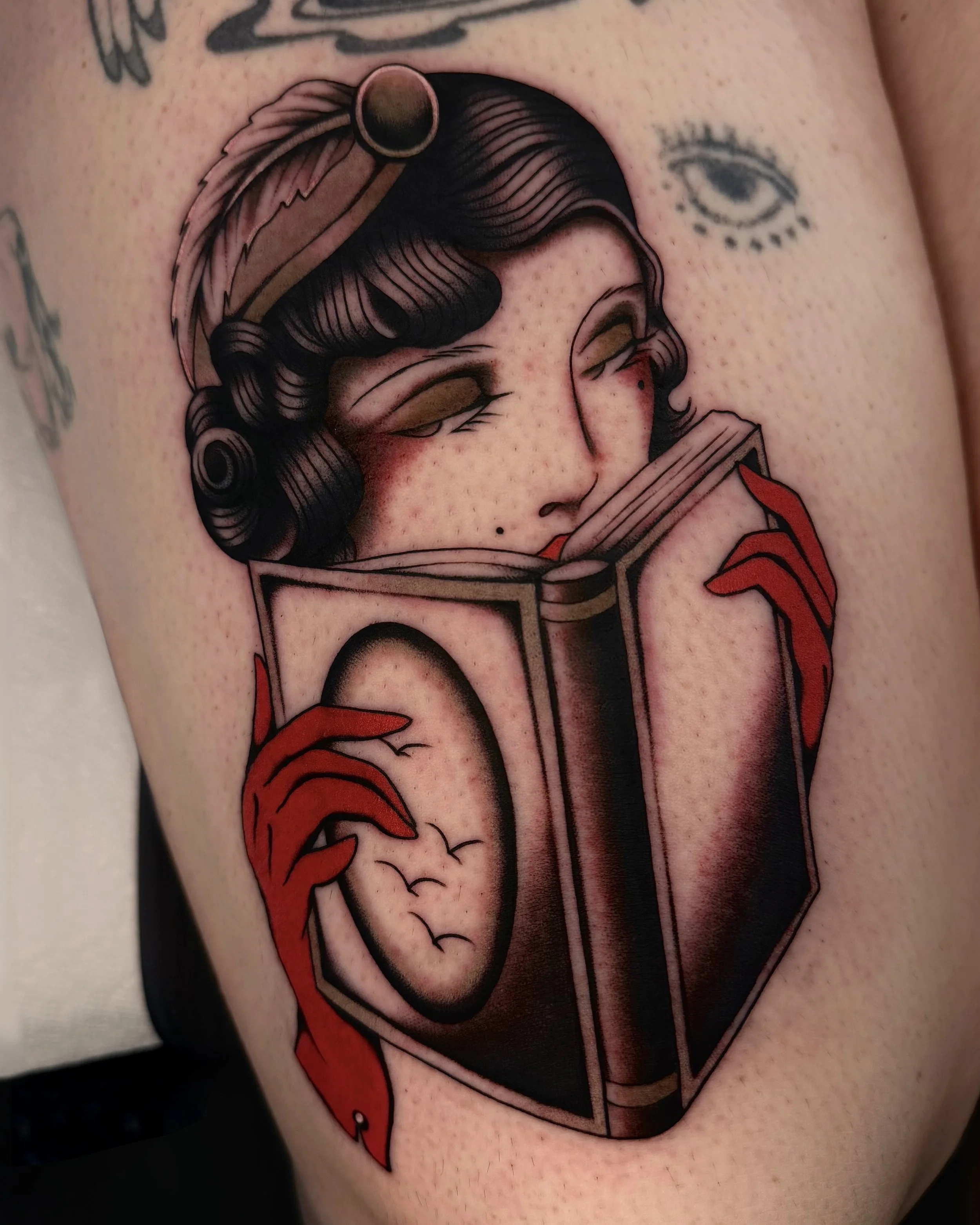 Tattoo of a woman's face and hair with a book, a feather, and a sun or moon in the background.