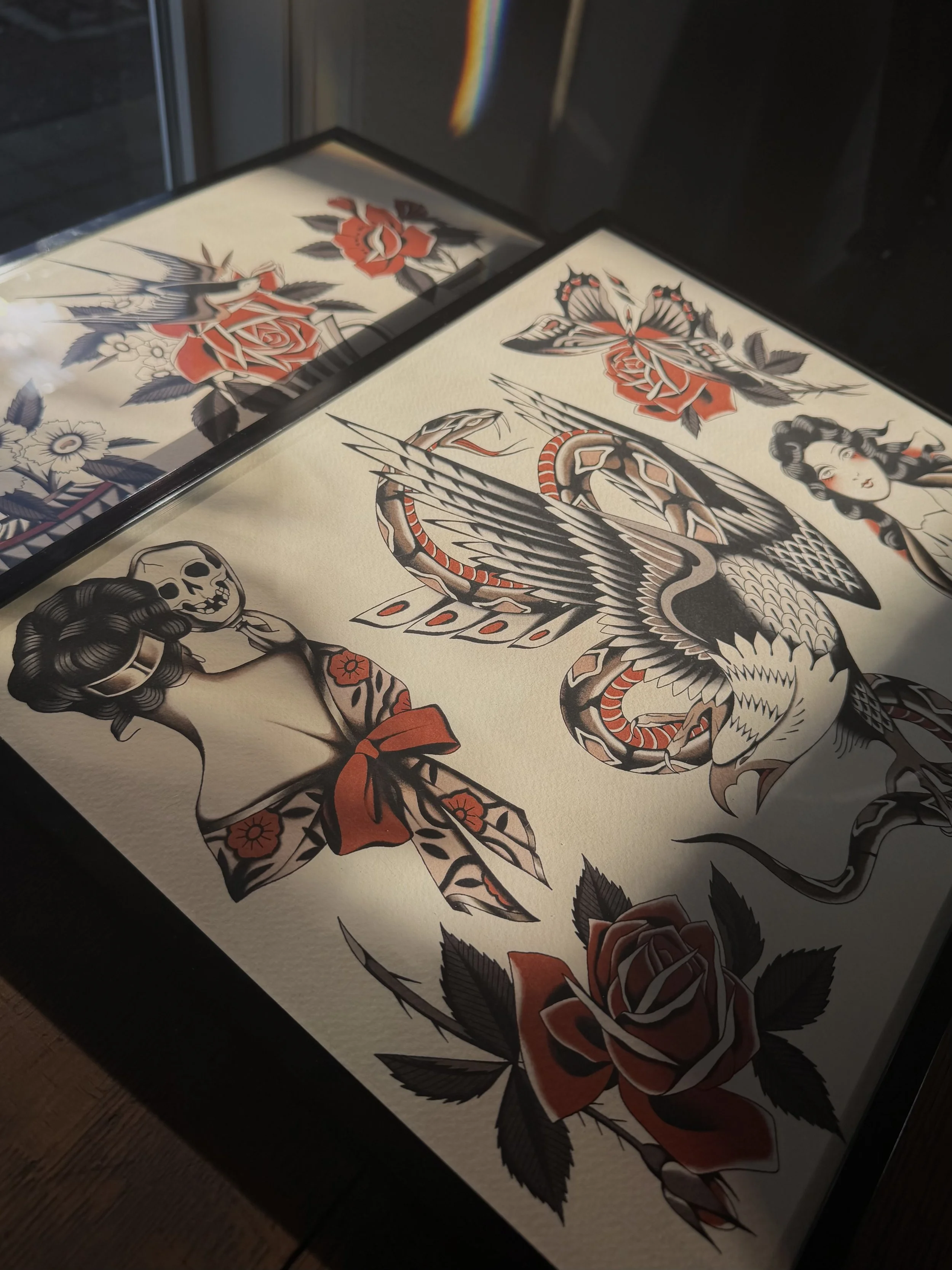 American Traditional tattoo flash in frames, by Donna Jean Tattoo at Deja Vu Tattoo in Portland Oregon. Tattoo designs of ladies, eagle and snake, roses, butterflies, and flowers