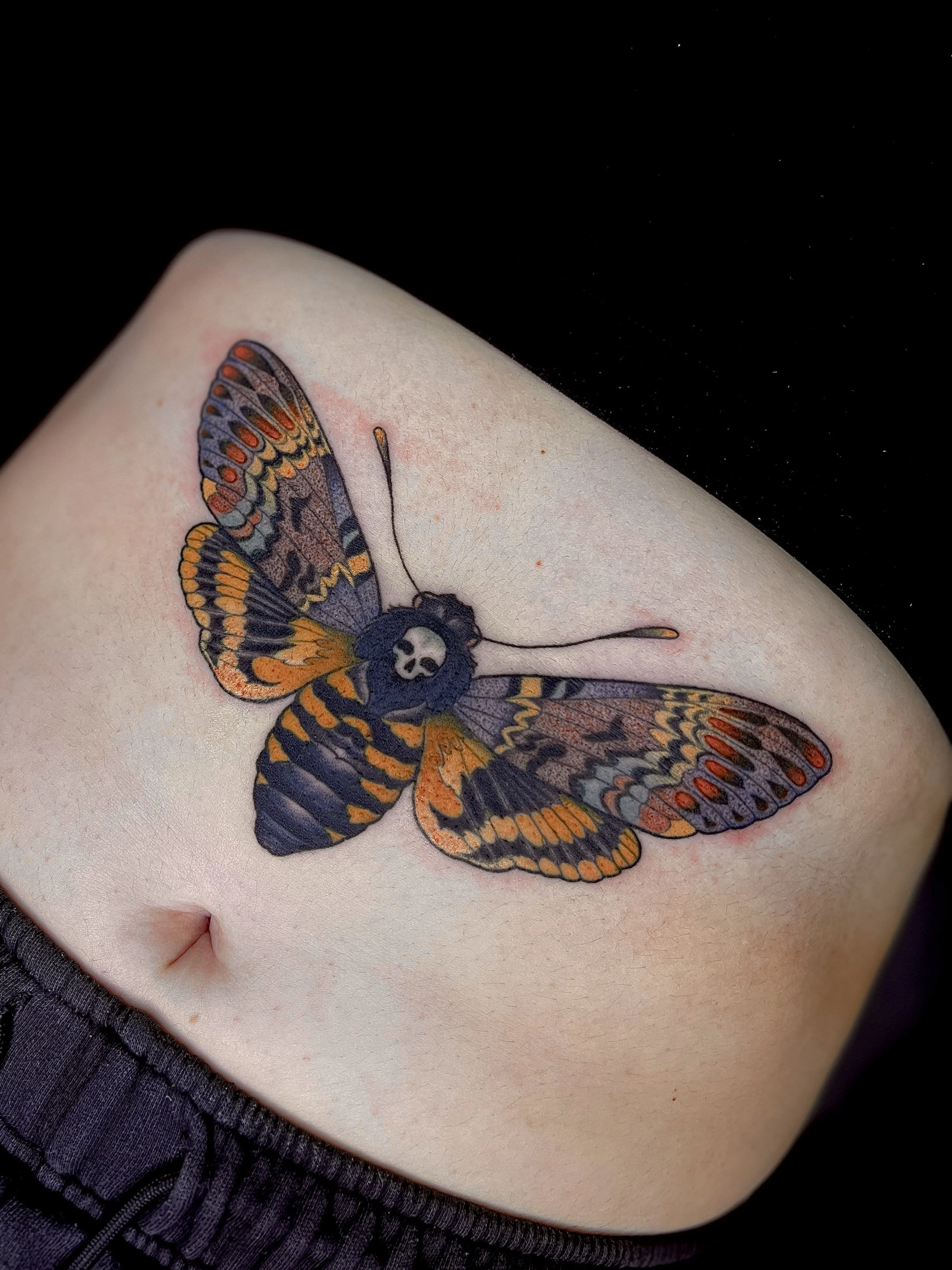 A tattoo of a colorful butterfly with detailed wings on a person's pale skin.
