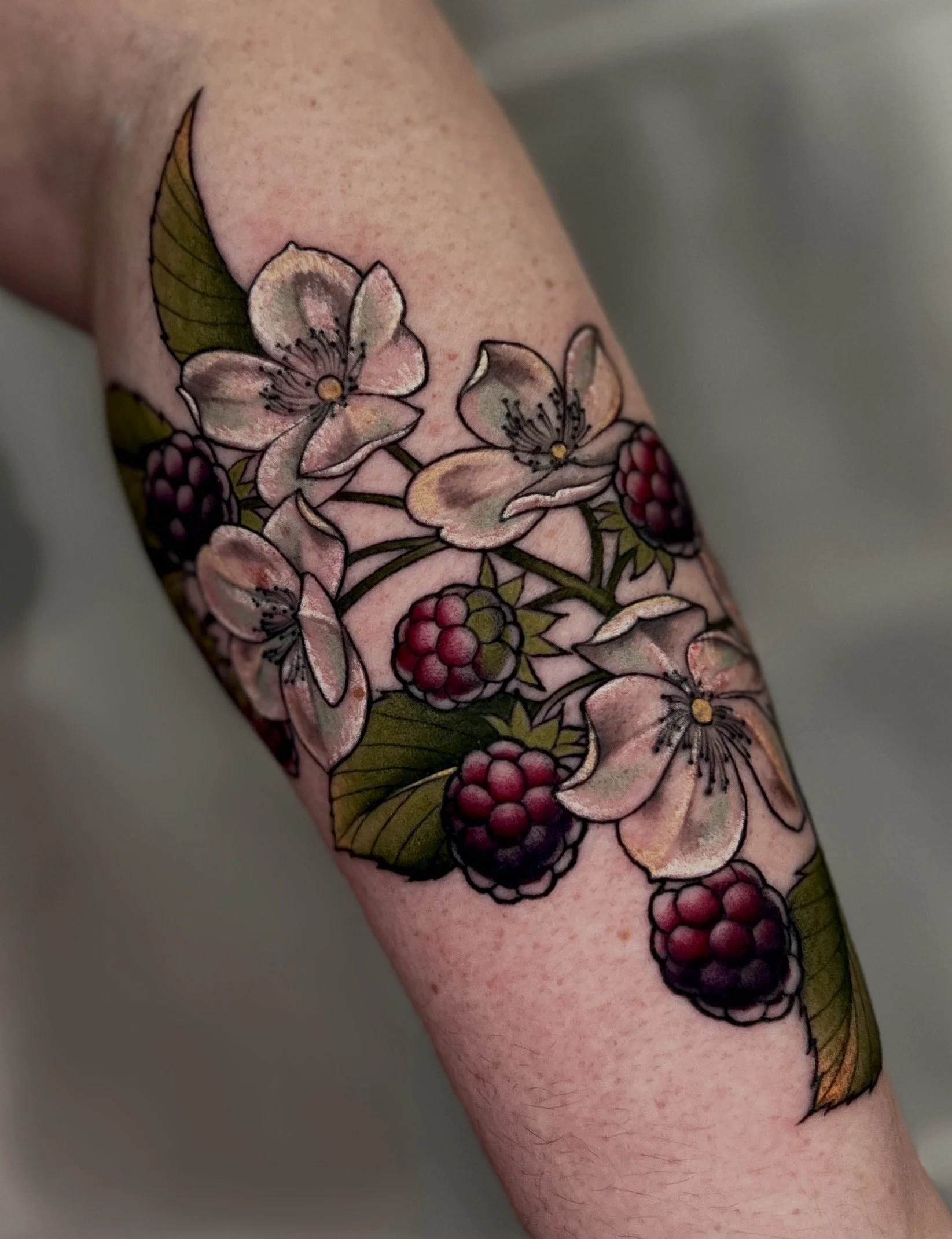 Close-up of a neotraditional tattoo of cherry blossoms and berries on a person's arm.