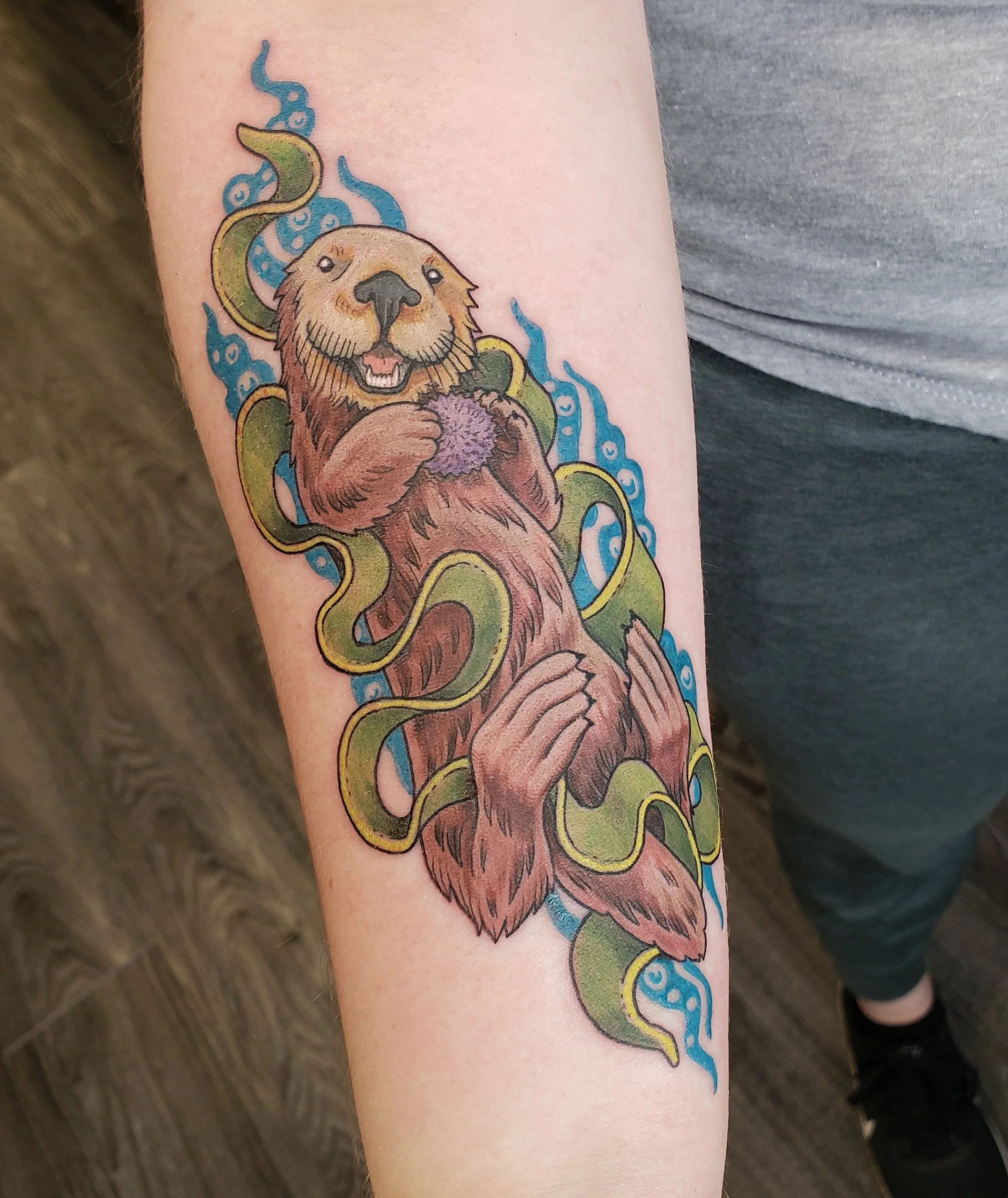 Colorful tattoo of a lion's face with a purple ball in its paws, surrounded by green and blue swirling smoke or flames.