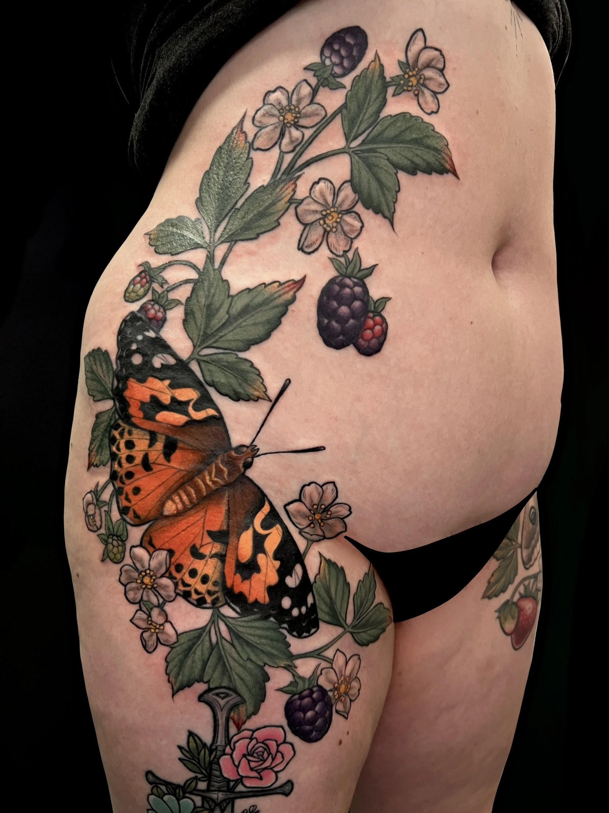 Colorful tattoo of blackberries, strawberry blossoms, a butterfly, and flowers on a person's upper arm and shoulder.