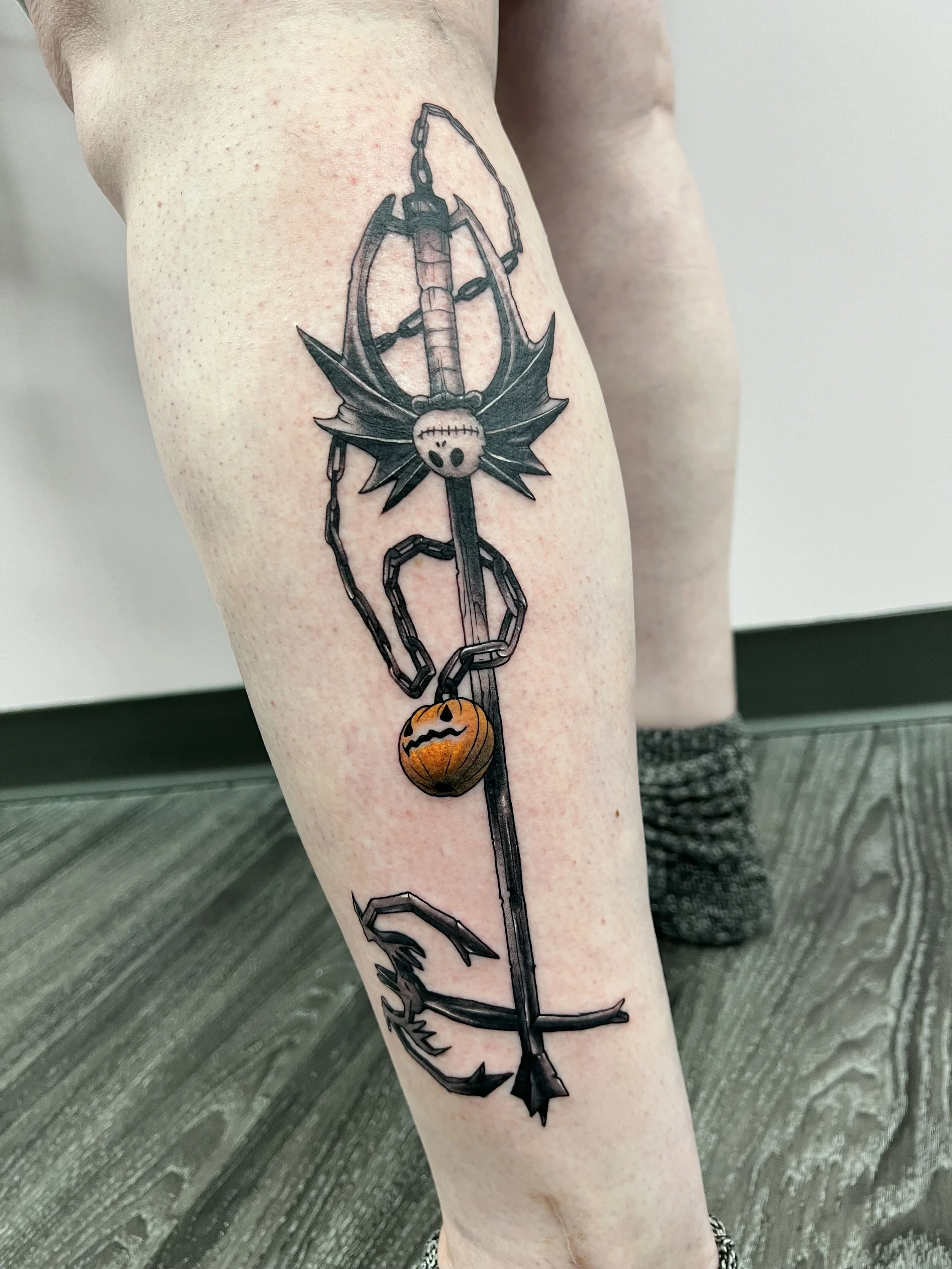 A tattoo of a Nightmare Before Christmas skeleton key from the game Kingdom Hearts, with a pumpkin and bat accent on a person's thigh.