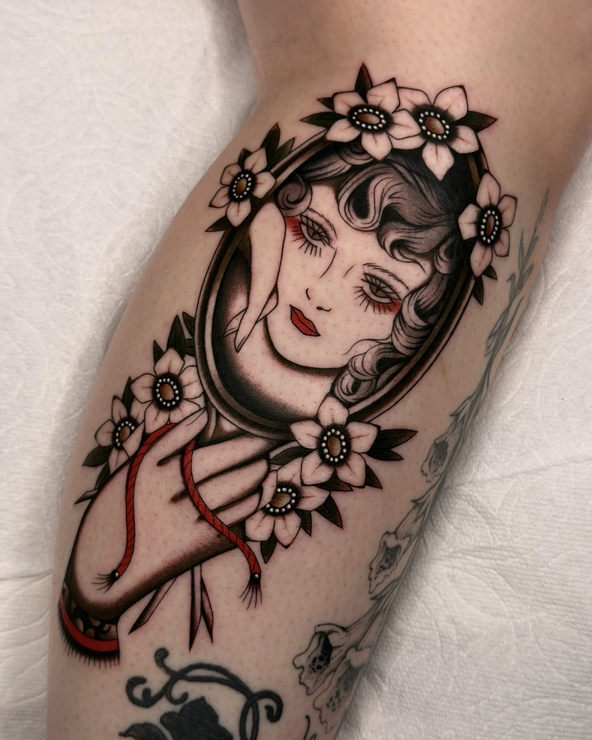 Classic Traditional Tattoo of a hand holding a mirror with a woman's face reflecting back, surrounded by white flowers