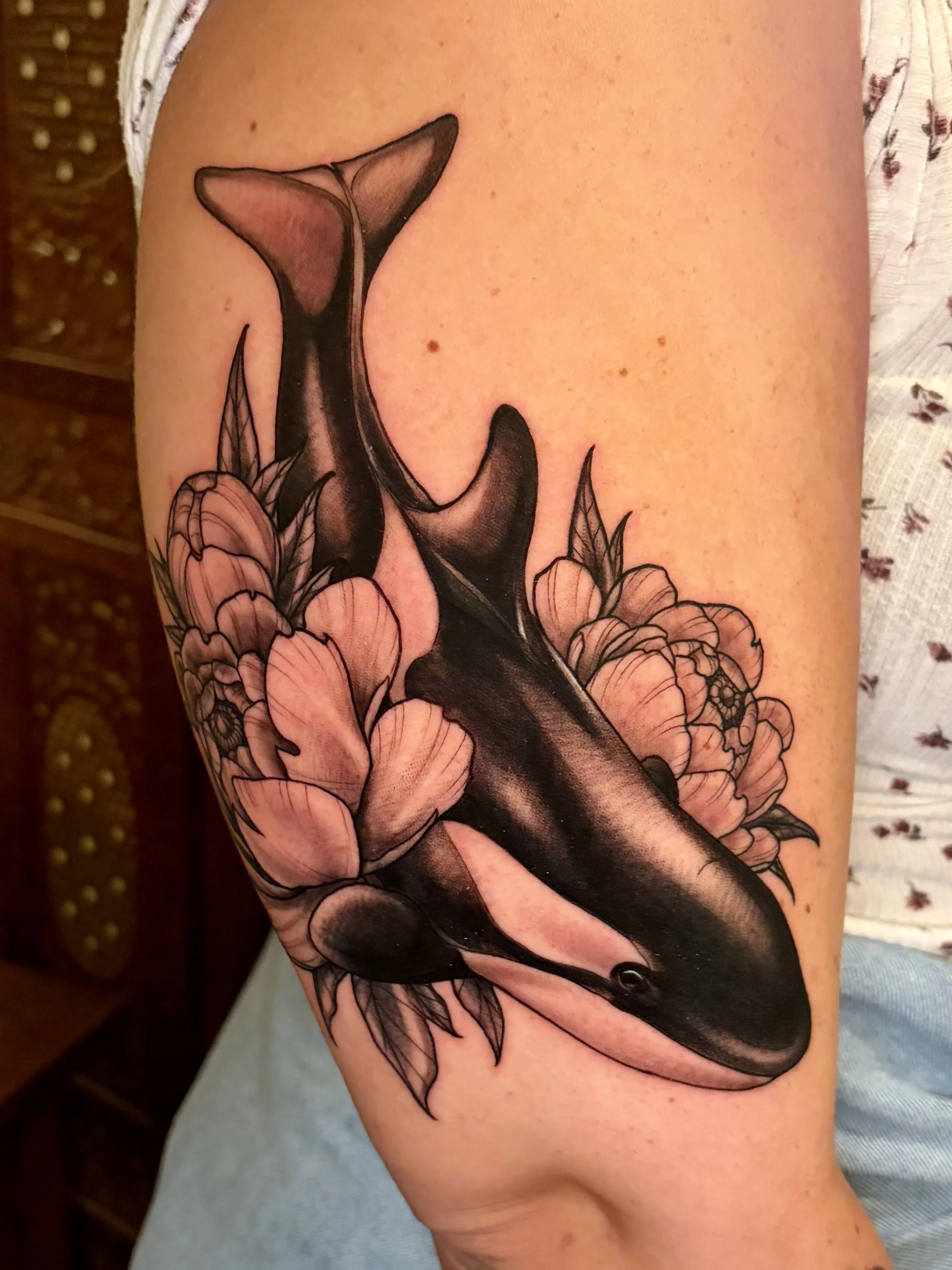 Tattoo of a killer whale surrounded by flowers on a person's arm.