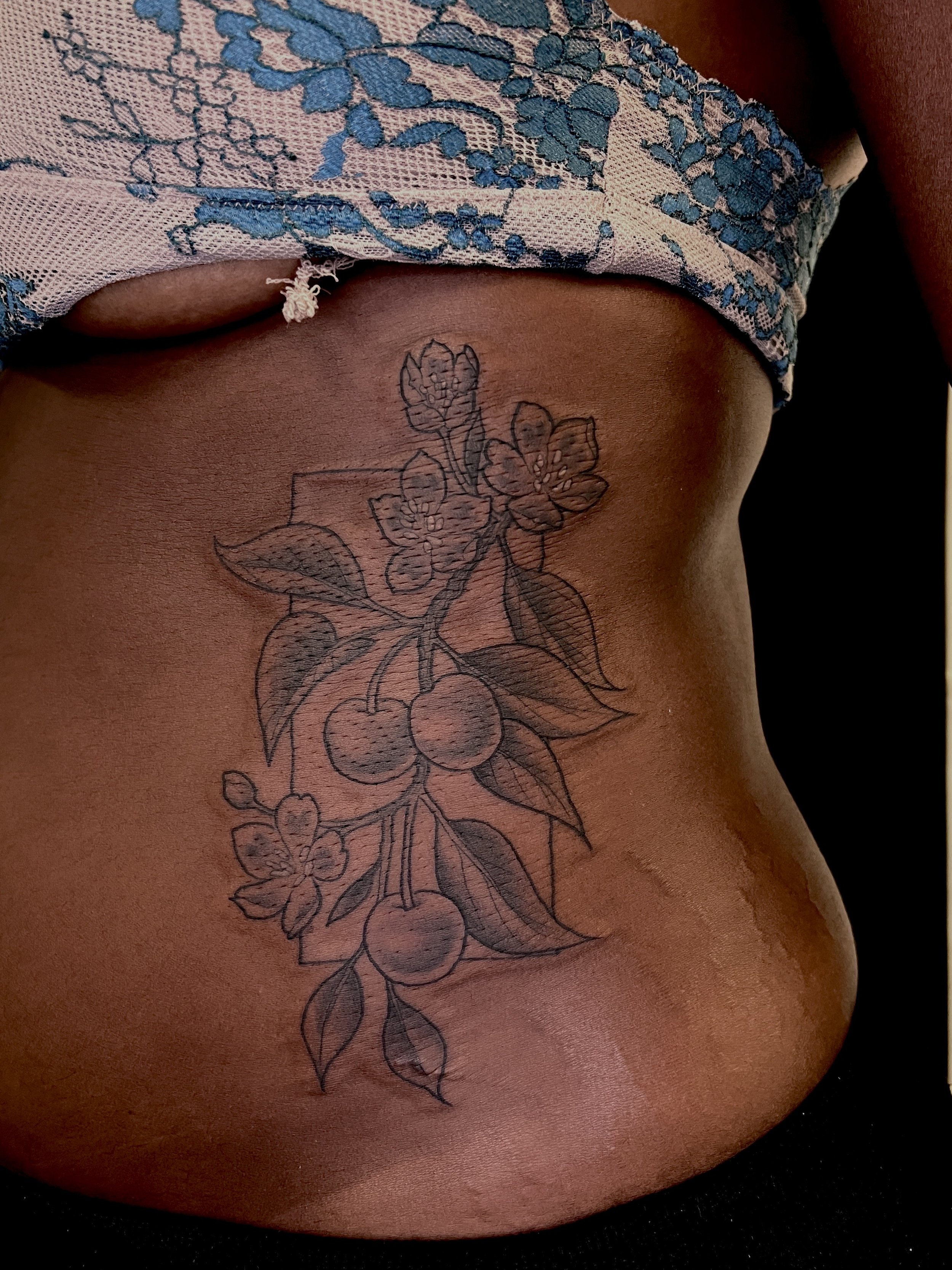 A close-up of a person's chest showing a black outline tattoo of cherries, leaves, and flowers.