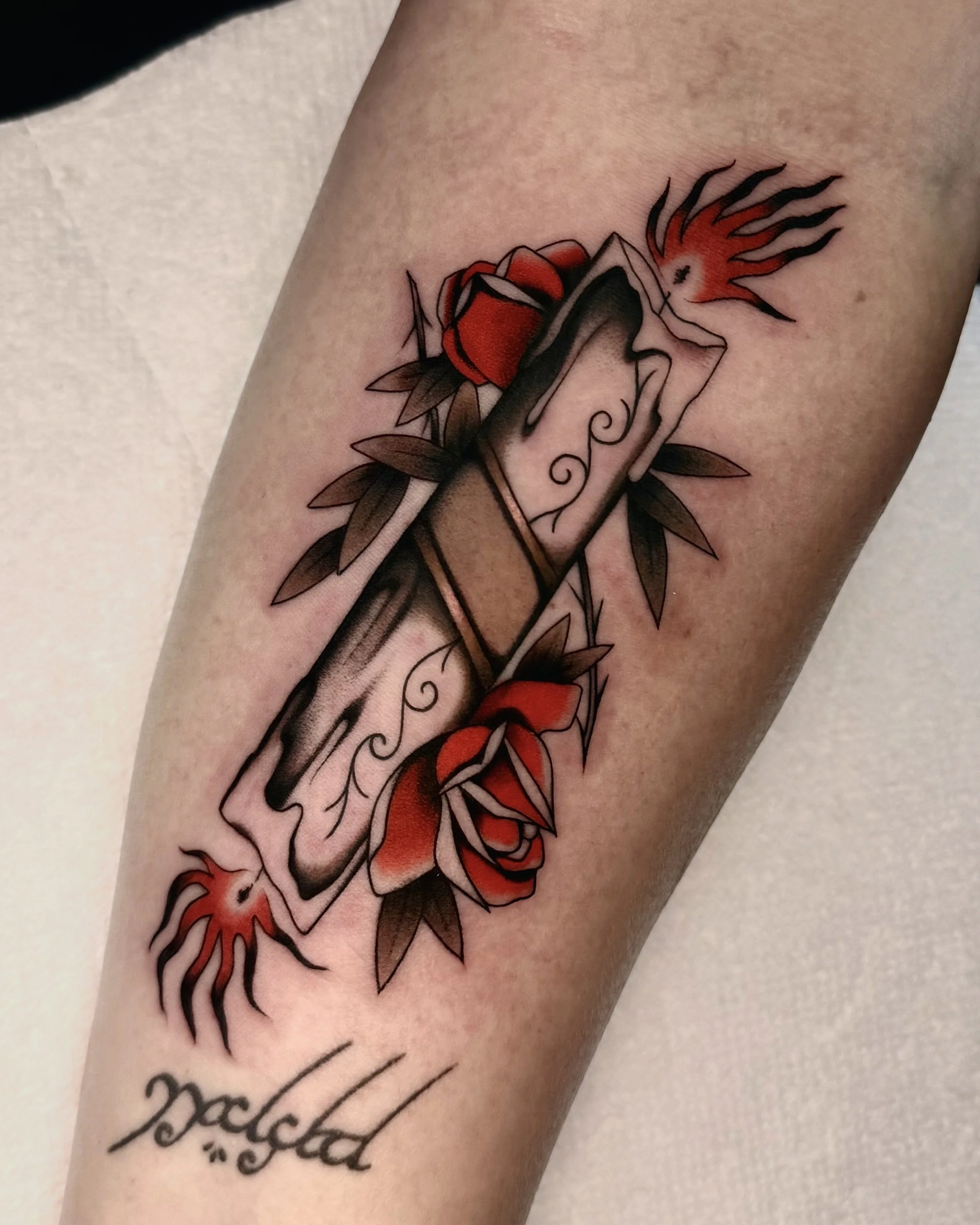 Tattoo of a red rose and a black and gray dagger with a fiery orange and black flame design on skin, with cursive script text partially visible below.