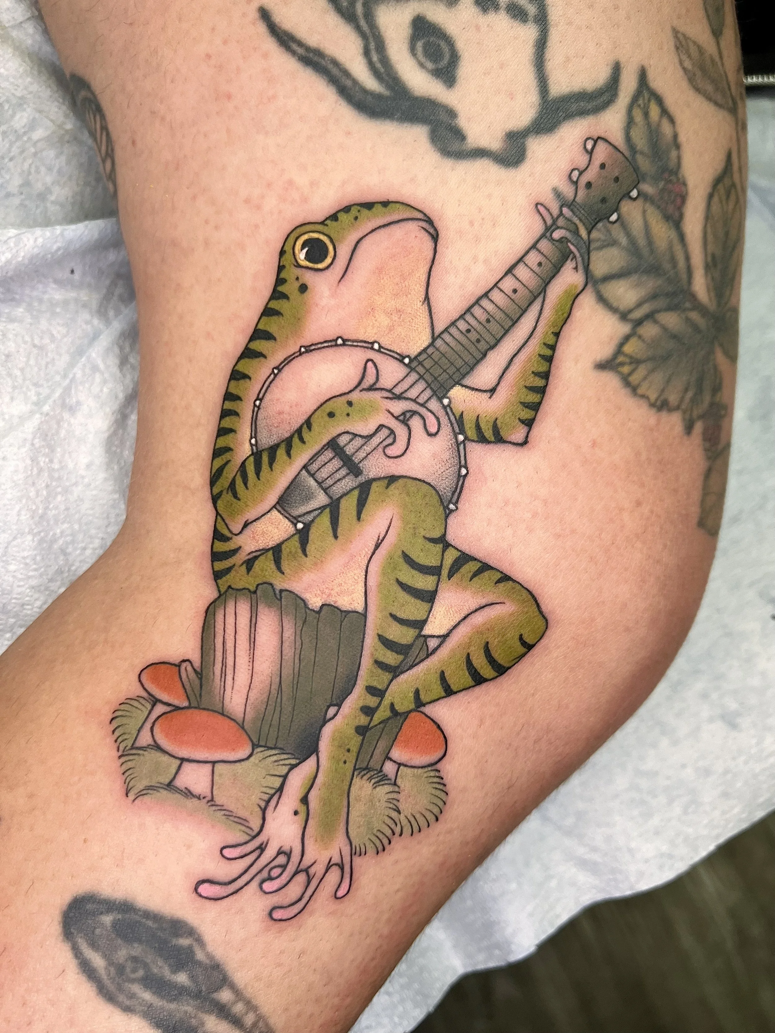 A tattoo of a lizard playing a banjo, situated on a person's arm.
