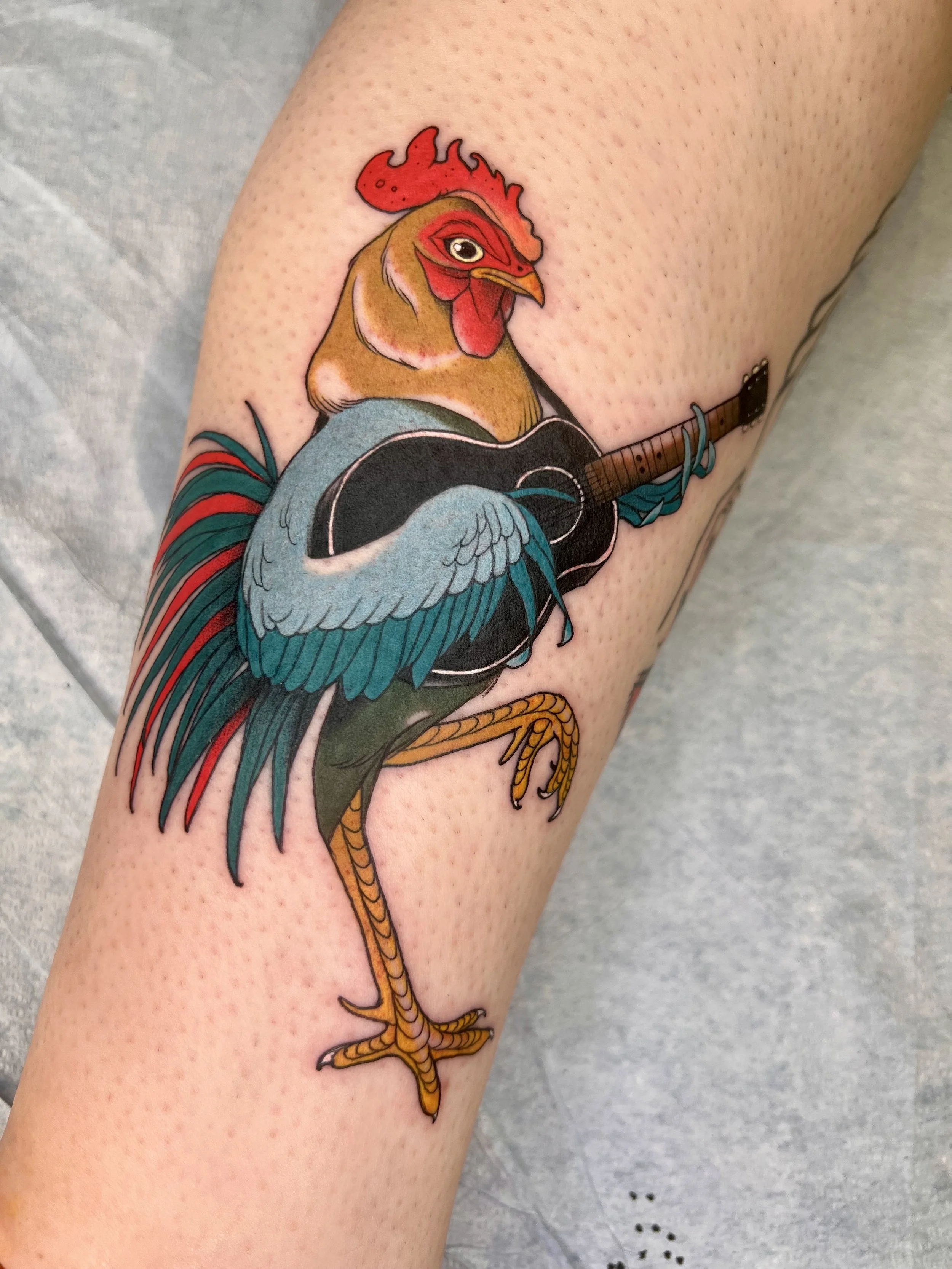 Colorful illustrative Tattoo of a rooster with a guitar on a person's arm.