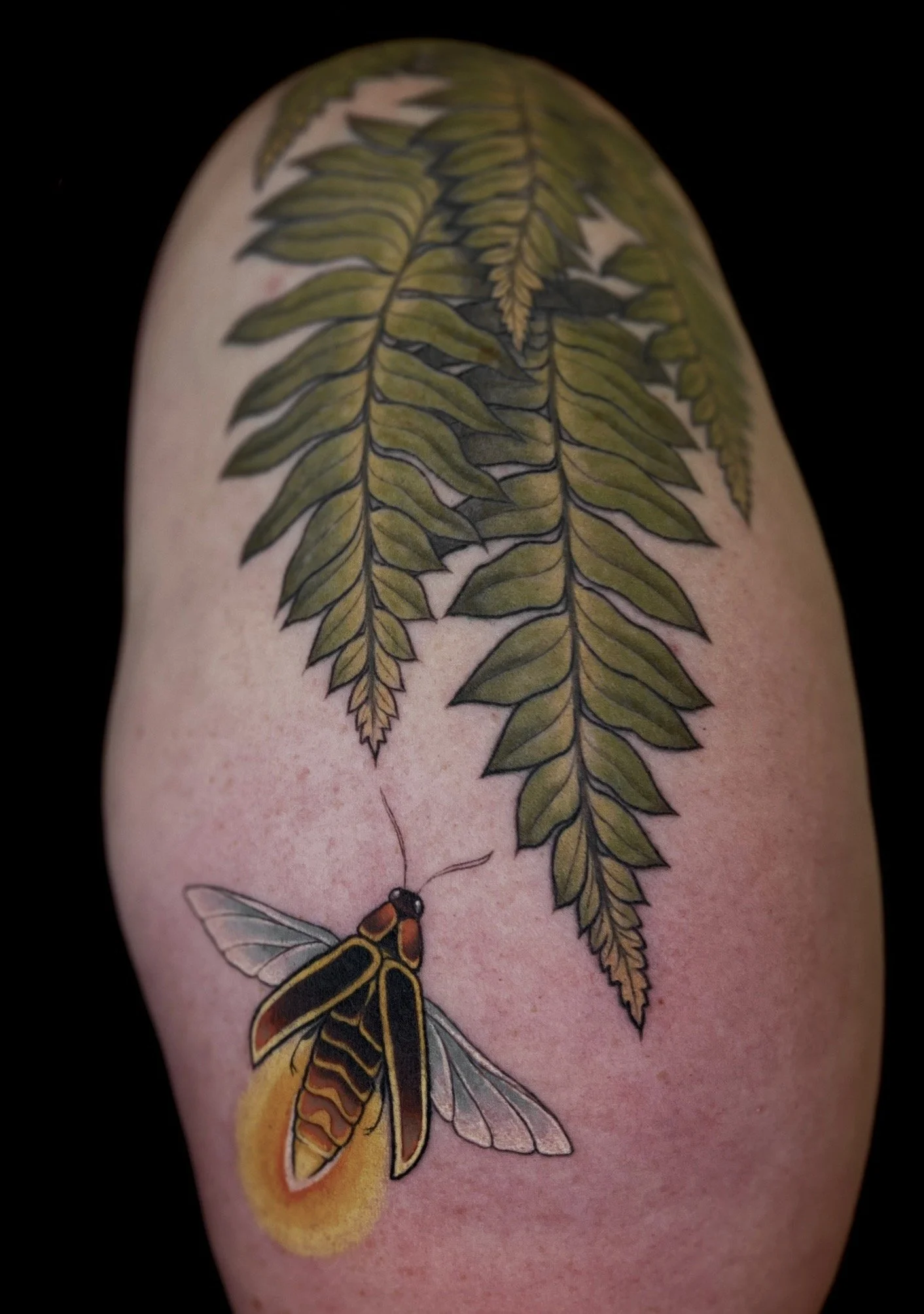 A tattoo of a fern branch with green leaves and a colorful bee with yellow, orange, and black markings on the skin.