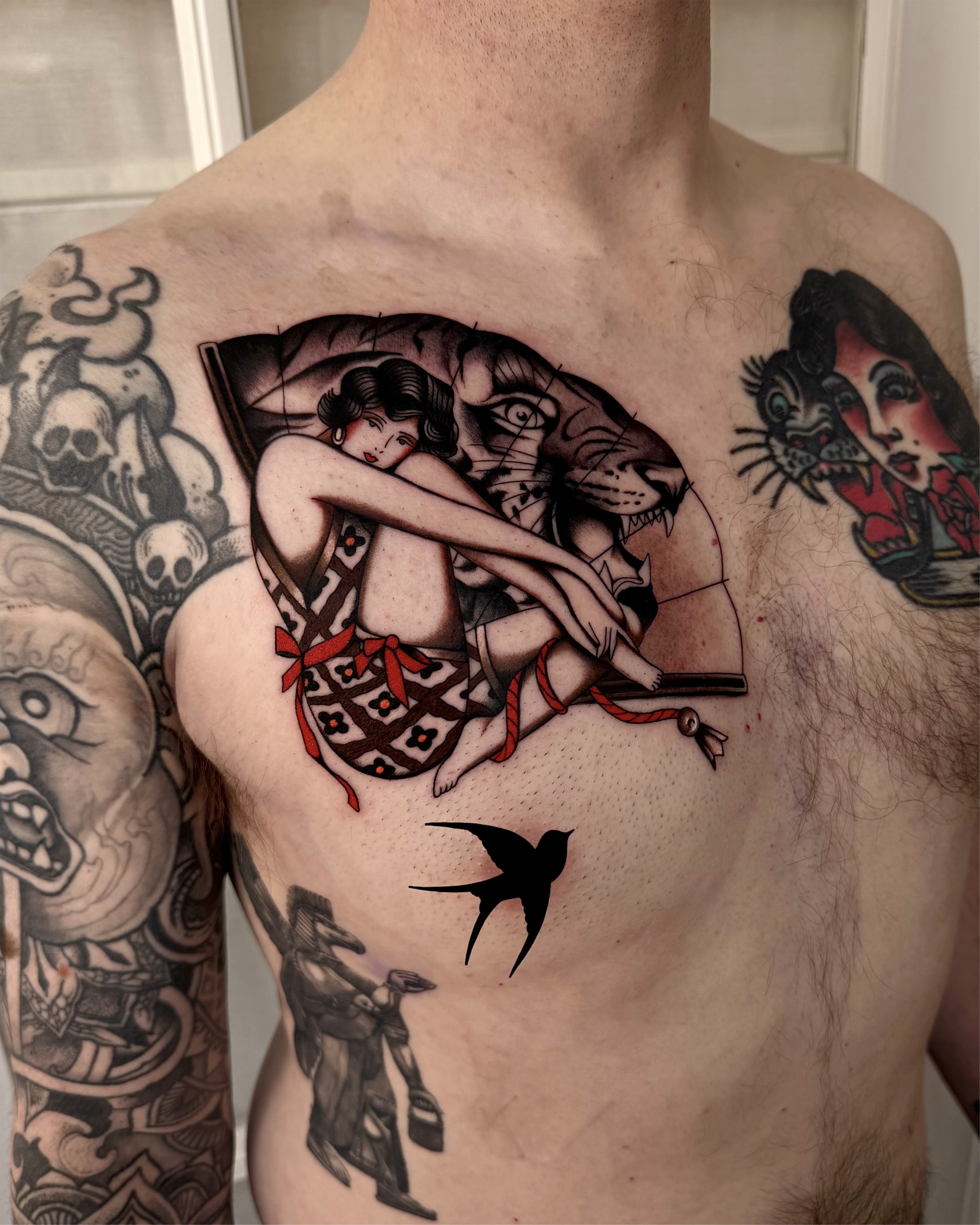 Tattoo of a woman with black hair and red lips sitting on a dagger, with a tiger's face behind her and a red bow on her dress. There is a black silhouette of a bird flying below the tattoo, on the person's side.